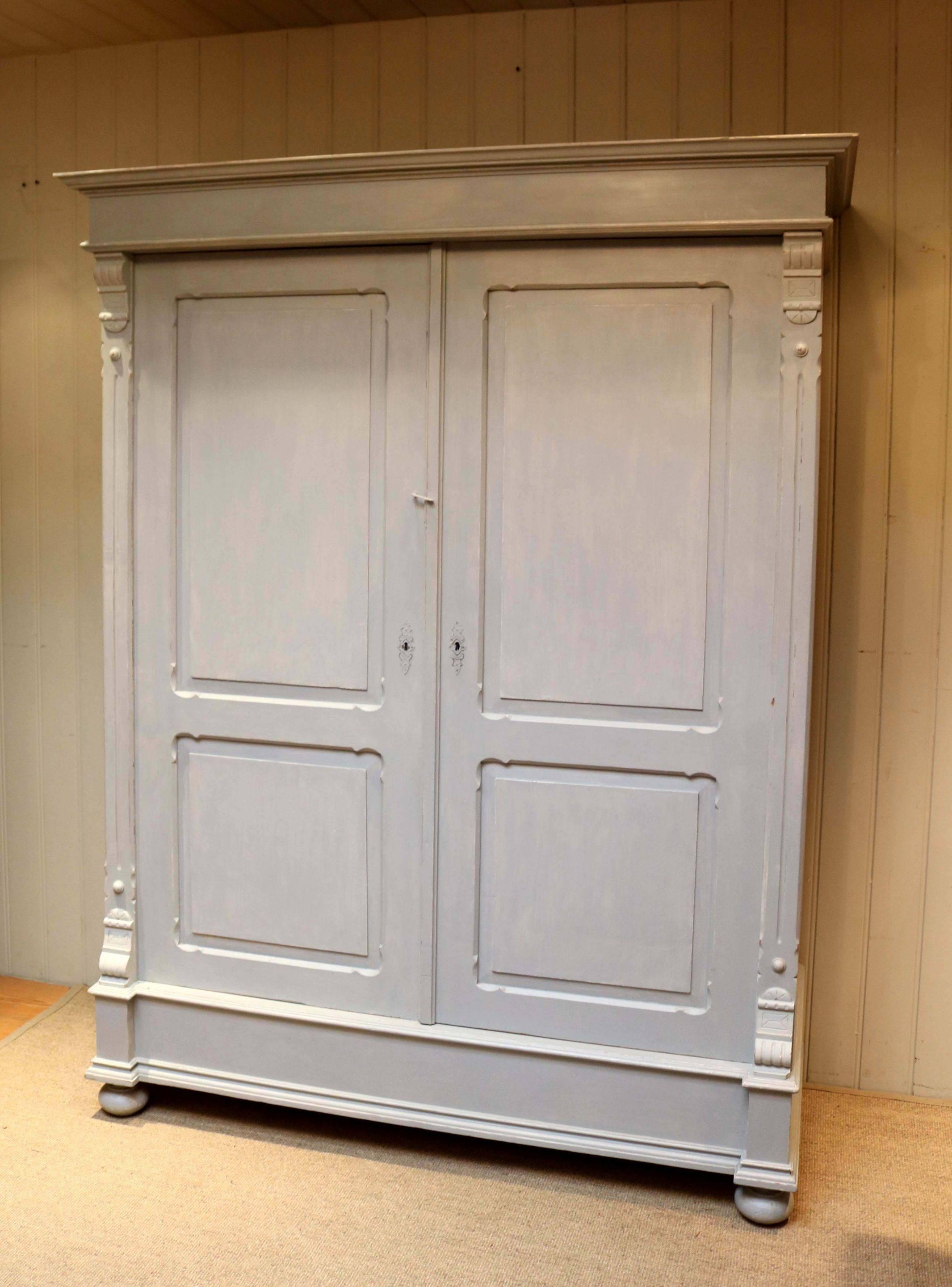 Large painted two-door wardrobe having panelled doors and carved side piliasters fitted internally with a shelf and hanging rail raised on turned wooden feet. This wardrobe dismantles for ease of movement.