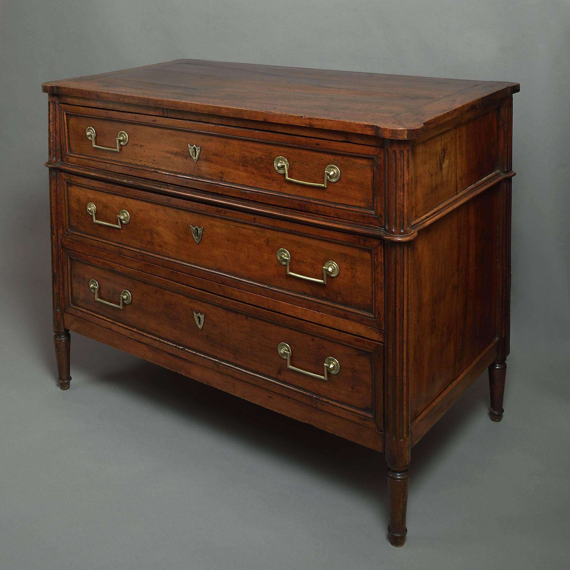 A late 18th century Louis XVI period walnut commode, having a cleated top above three drawers with rectangular brass handles and shield lock escutcheons, between fluted column ends, all raised on turned legs.