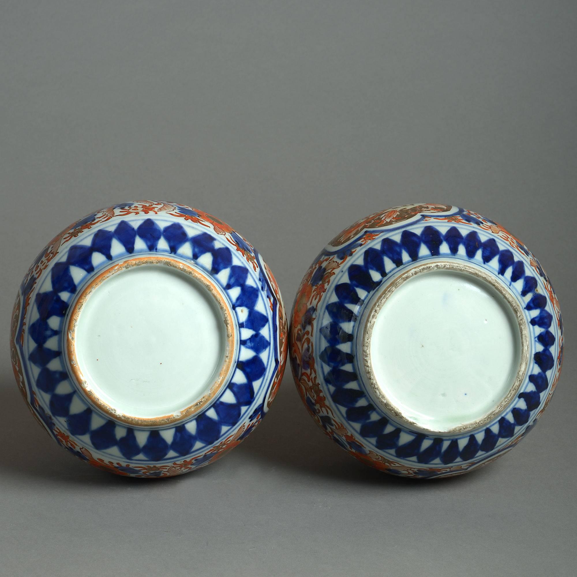 A late 19th century pair of Imari porcelain bottle vases, the bulbous bodies having long stems and decorated throughout in red, blue and gold glazes upon white grounds. 

Meiji period (1868-1912).