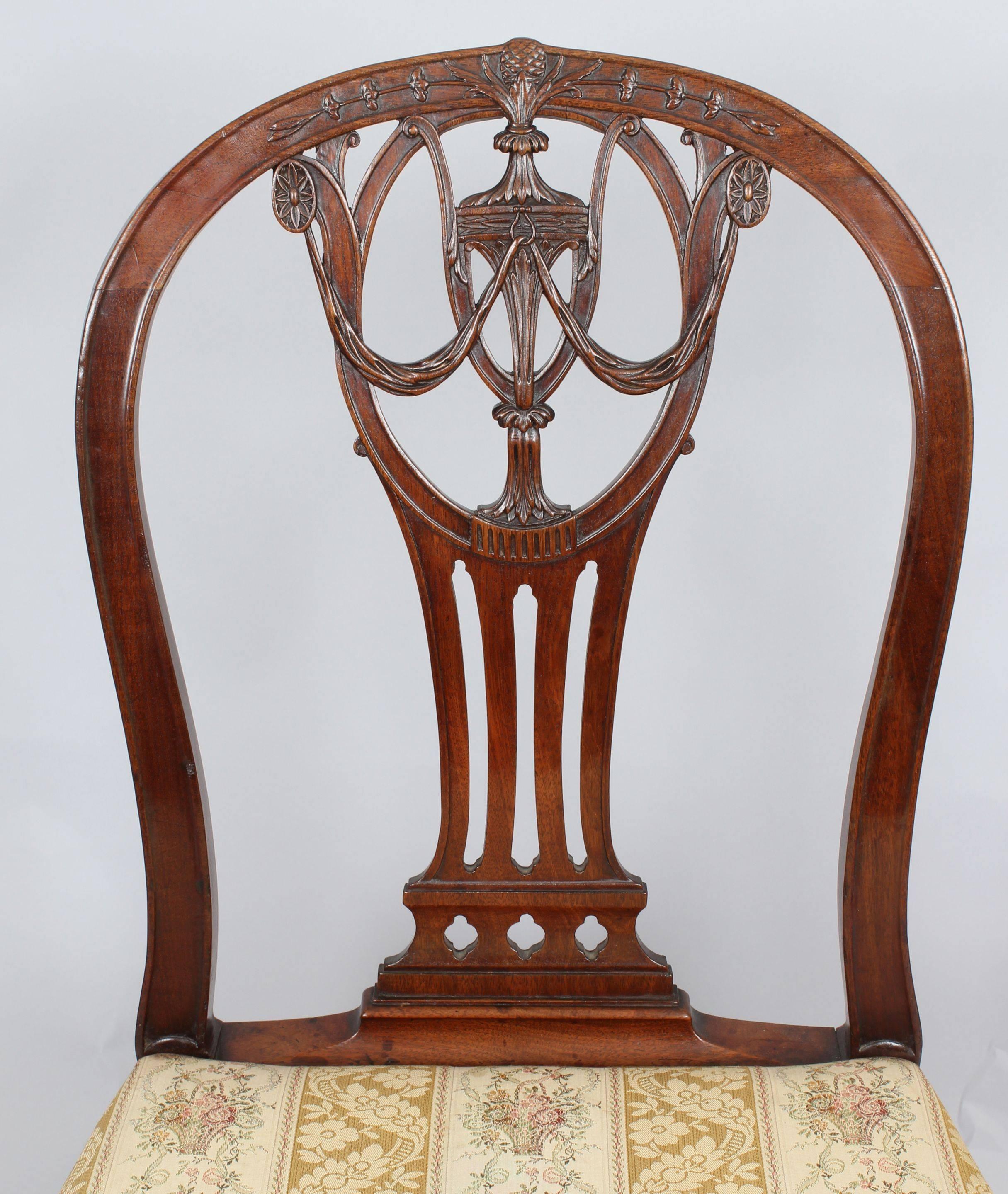 Pair of George III period mahogany side-chairs in the Hepplewhite manner with channelled arched backs and finely-carved openwork splats decorated with a central urn, drapery, oval paterae, floral trails and a pine-cone cresting. The bowed seats with