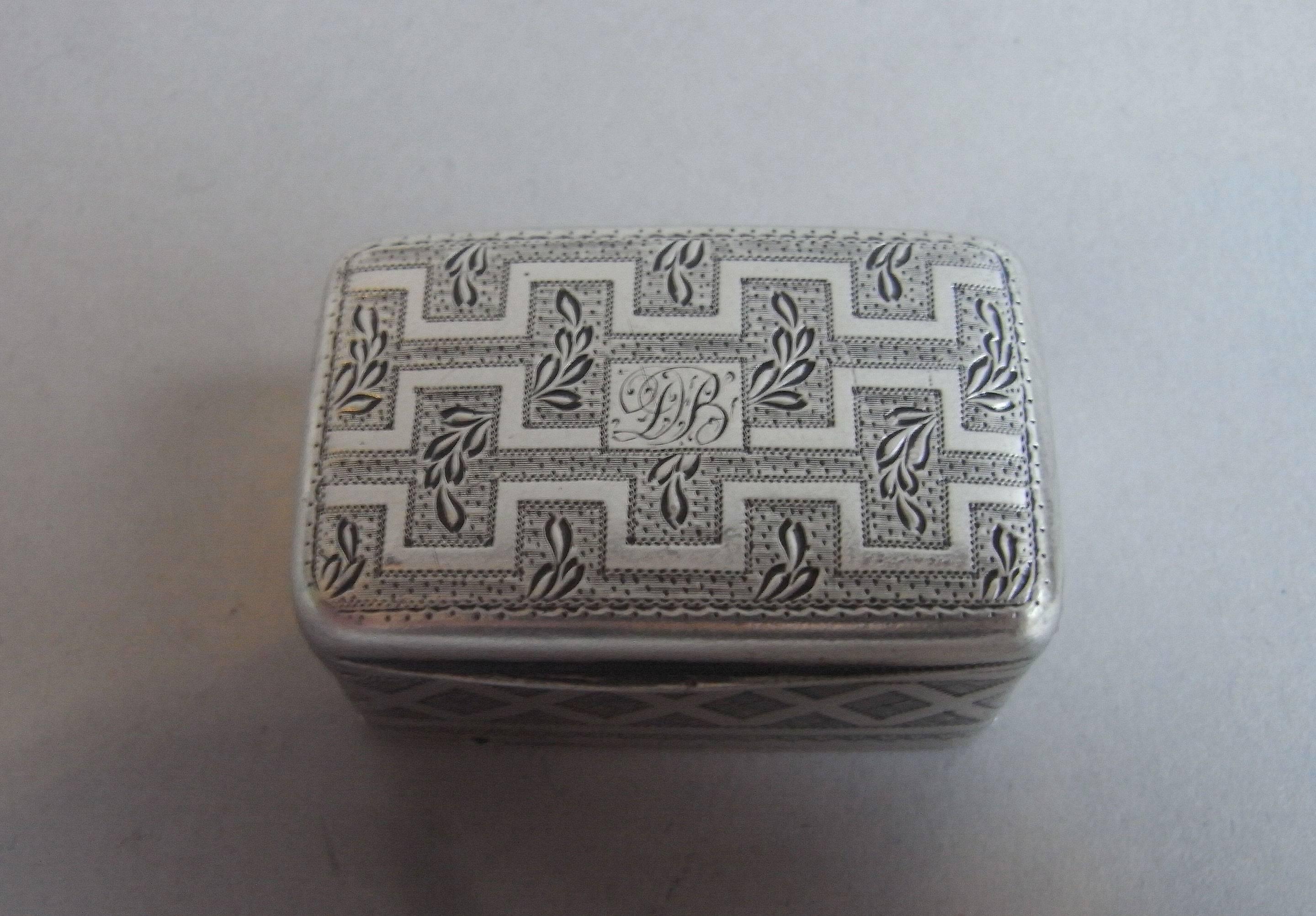 The nutmeg grater is broad rectangular in form and the cover and base are beautifully engraved with two bands of Greek key designs surrounded by a prick dot ground and unusual bright cut stylized foliate motifs. The engraving is particularly