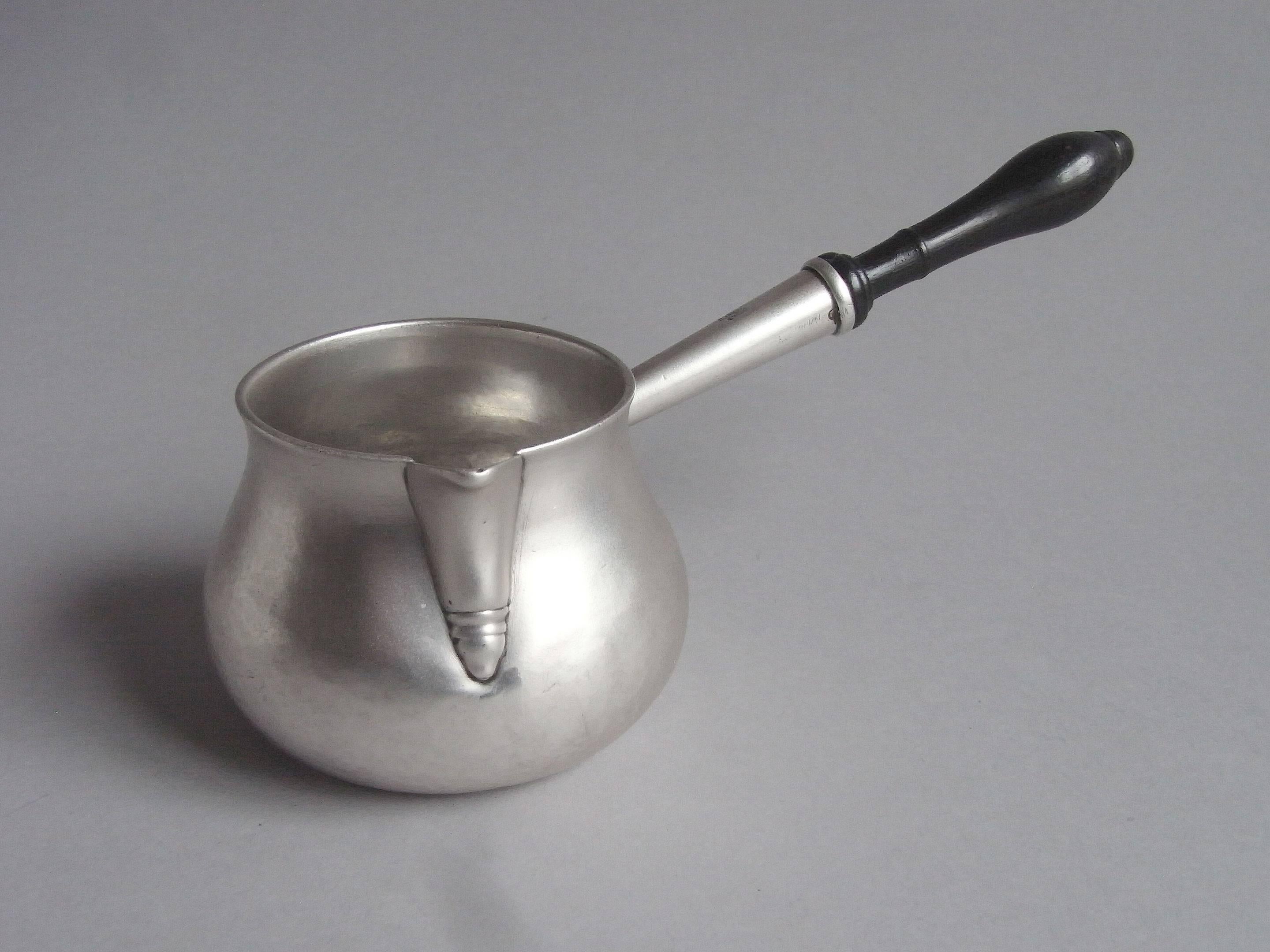 The saucepan is of a small size and has a baluster shaped body rising to an everted rim. The sparrow beak spout is decorated with a double drop below and the silver section of the handle is attached to the main body with a heart shaped molding and