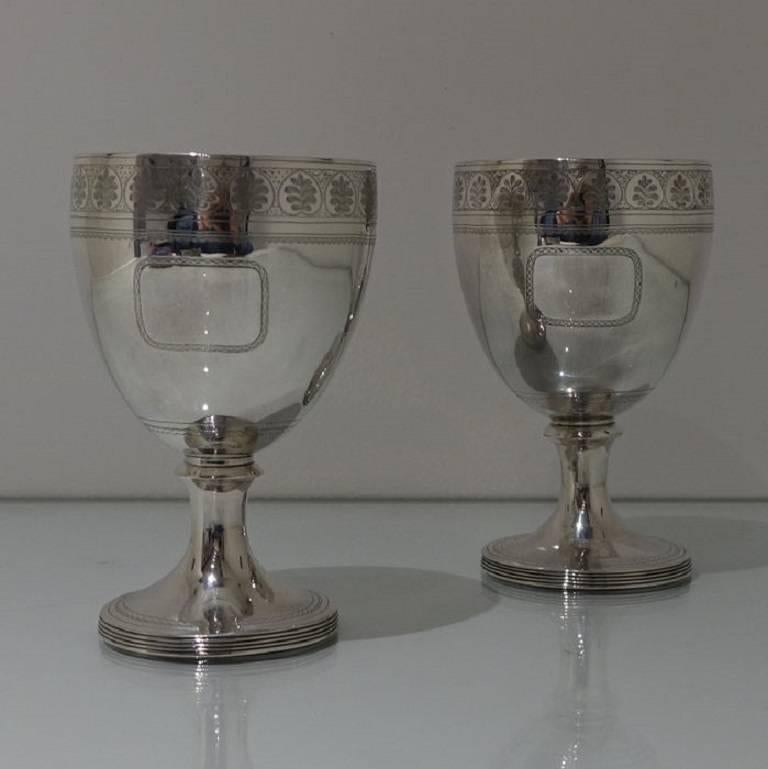 A pair of early 19th century wine goblets with a band of stylish floral bright cut engraving around the rim of the lip. The centre front of the bowl has an elegant cartouche. The foot has a reed bezel with an additional band of bright cut engraving