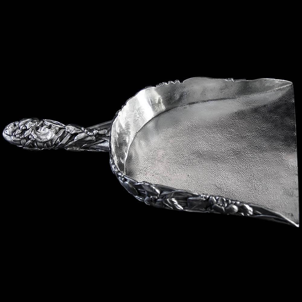 A Decorative silver crumb scoop in the form of a brush pan. The sides and handle decorated with heavy floral design and the scoop pan with hand hammered finish. Kuhn & Komor were one of the few companies in Japan warranted to make decorative