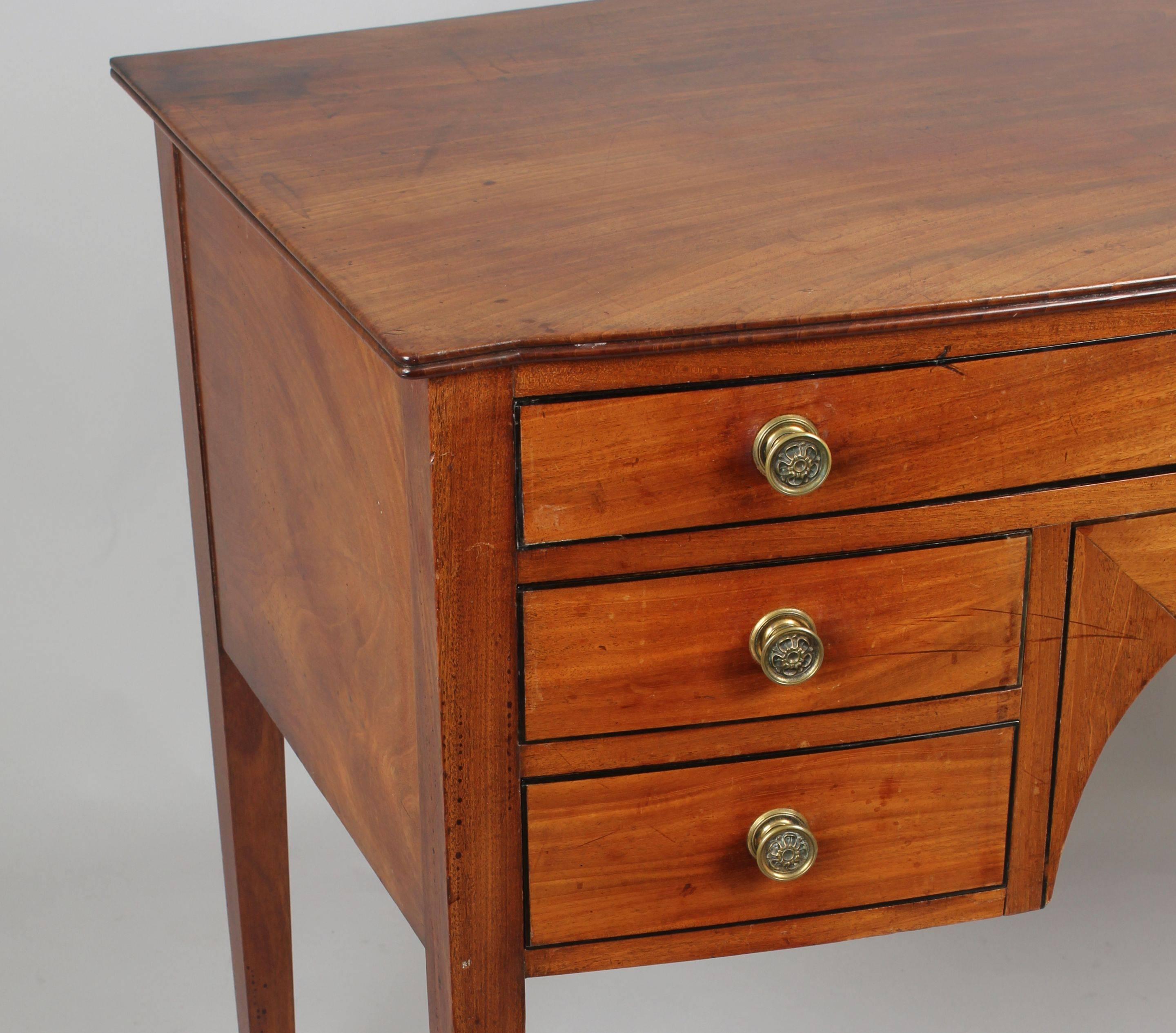 George III period faded mahogany small bow-fronted sideboard; the top with a reeded edge and the drawers with ebony strung borders and their original brass knob handles; the long top-drawer divided and lined with green baize for cutlery; on square