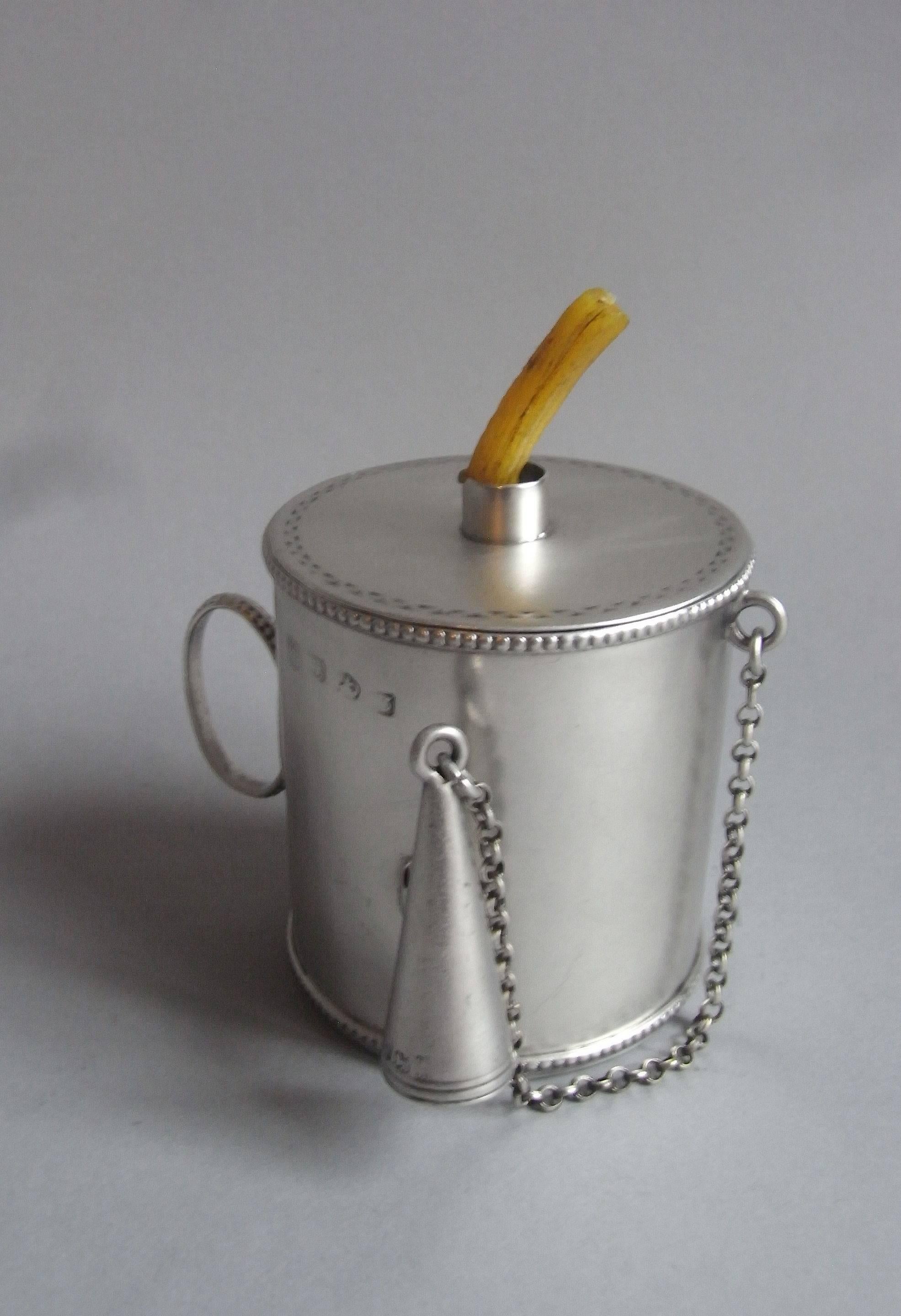 The Bougie box is of circular drum form with a beaded rim and base. This example displays a very unusual beaded loop carrying handle. The detachable cover has a bright cut rim and the reeded conical extinguisher is attached to the side of the main