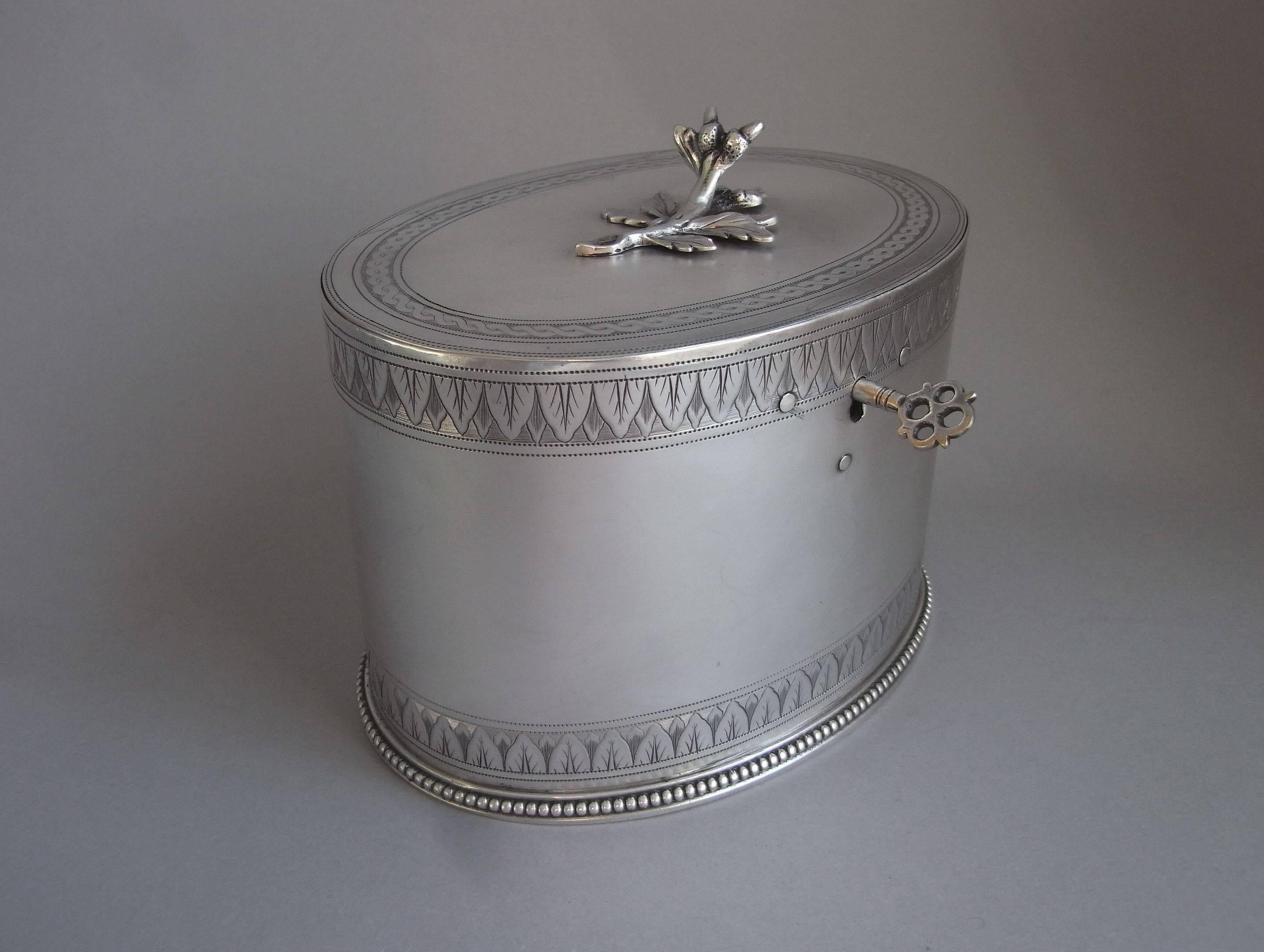 The tea caddy is oval in form with a beaded base. The sides display two very unusual horizontal bands of engraving depicting foliate motifs in sizes, the first time we have seen this design coming from Hester's workshops. The rear of the tea caddy
