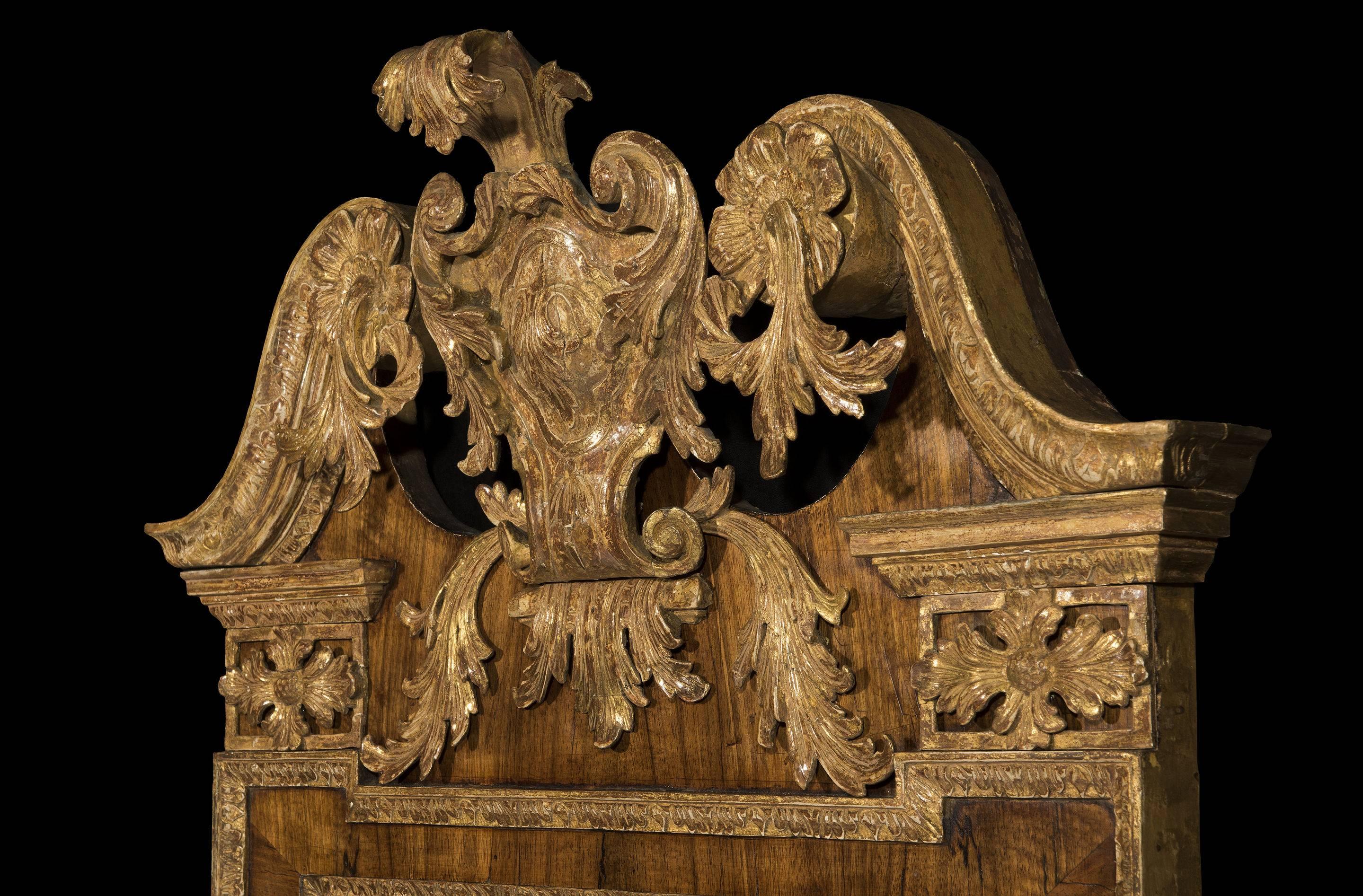 The top of the mirror has a pair of intricately leaf-carved giltwood swan-neck pediments each terminating in a flower rosette with trailing leaves. The centre crest with a scrolling leaf pediment and 'C' scrolled decoration is surmounted on a walnut