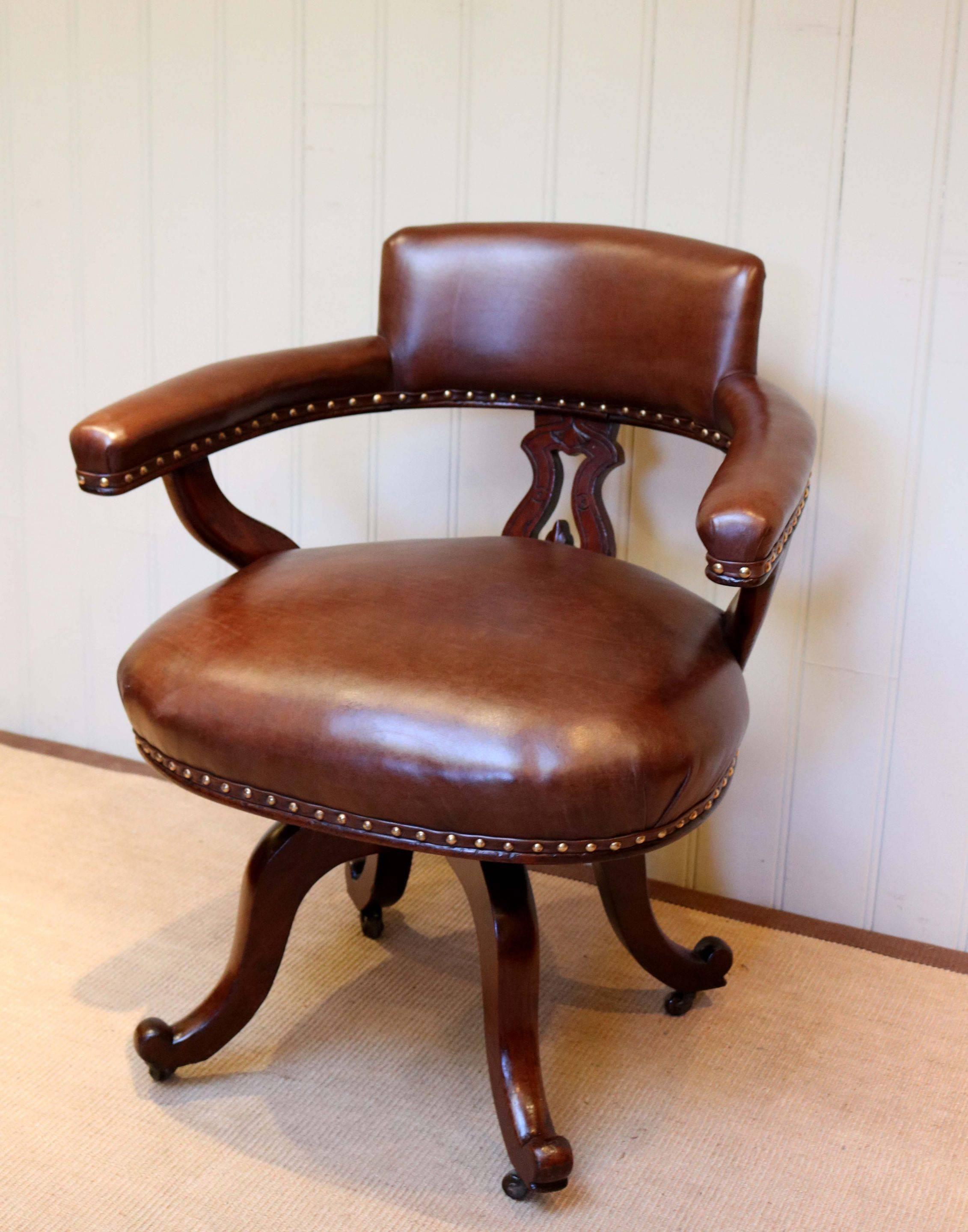 Victorian mahogany and leather desk chair with a nicely carved back support and upholstered arm rests on a swivel quadraform base with ceramic castors, reupholstered in high grade leather with brass studs.
