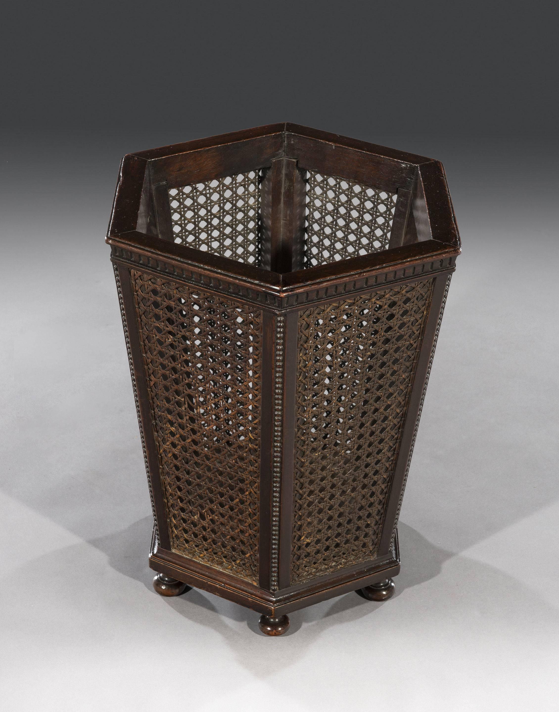 The octagonal mahogany waste paper basket has etched markings above caned panelled sides and mahogany upright supports with bobbin mouldings. The waste paper basket stands on turned mahogany bun feet.