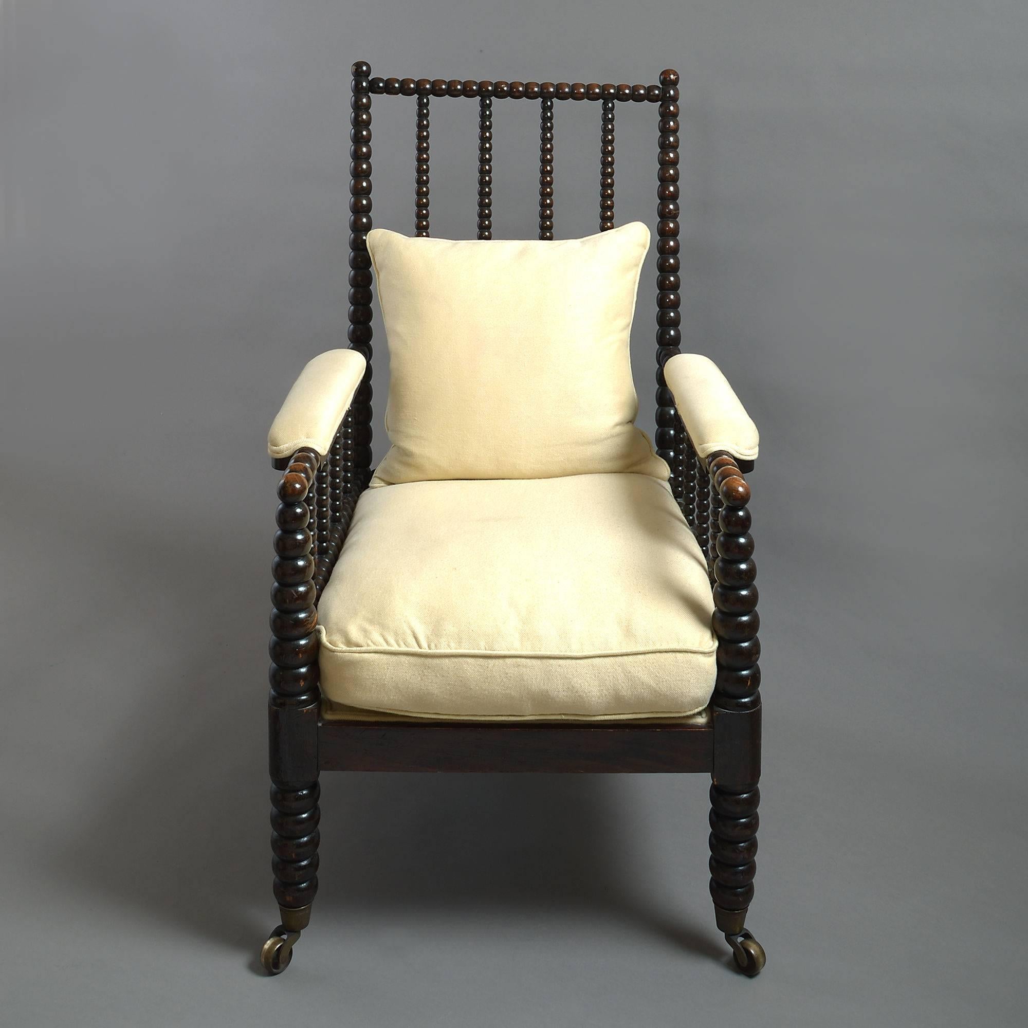 A large-scale mid-19th century ebonized bobbin turned spindle armchair, with upholstered arms and cushion seat, raised on the original brass castors.