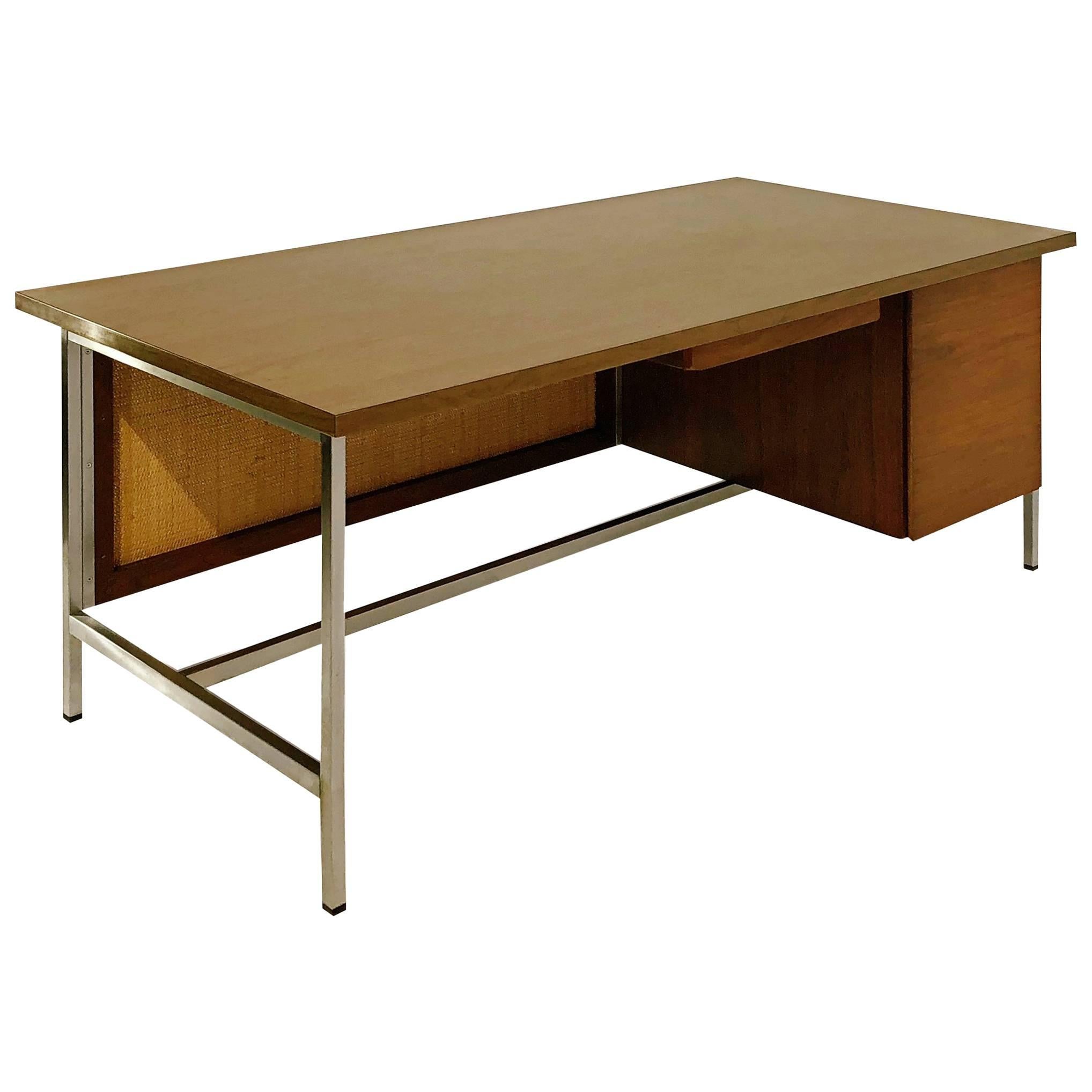 Expansive executive desk by Florence Knoll. This unique example is fabricated from walnut with an attractive grain and features a kneehole modesty panel that is decorated with a George Nelson / Herman Miller style caning on the reverse. Underneath