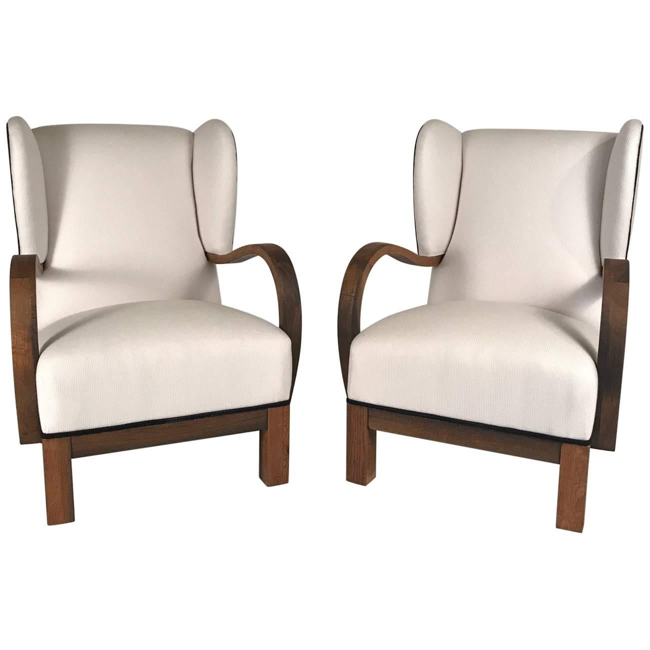 Handsome, sturdy pair of Danish modern wing-back open armchairs with exaggeratedly curved arms in oak
reupholstered in white fabric with black trim, art deco period.