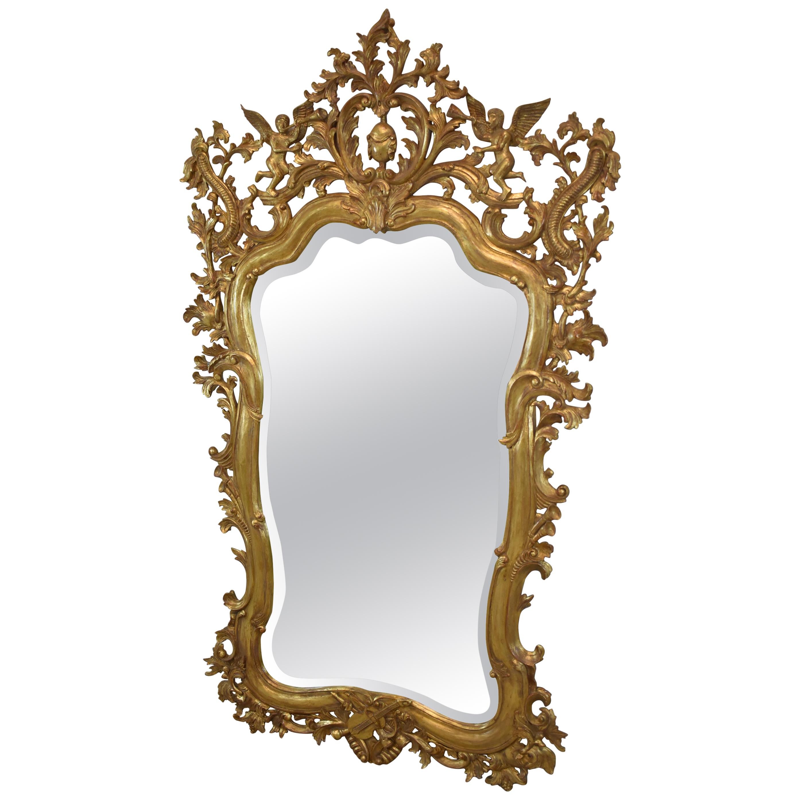 Miroir italien en bois sculpté et doré représentant des anges qui trompent, biseauté