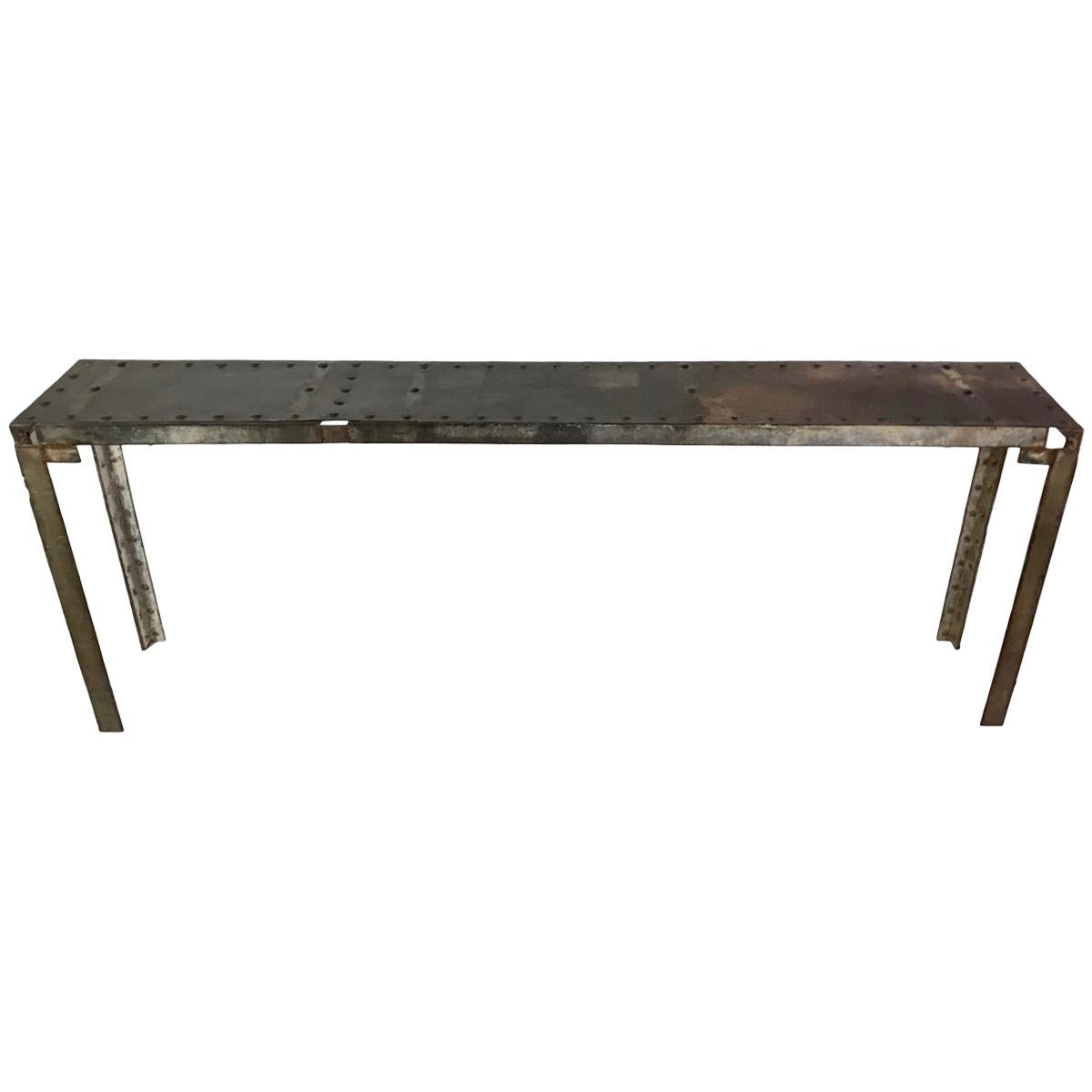 This is a fantastic Industrial steel console from France, circa 1940. There are oversized steel rivets along the top, edges, and down the legs. One side of the console has an arch detail on either side, whereas the other side shows an interesting