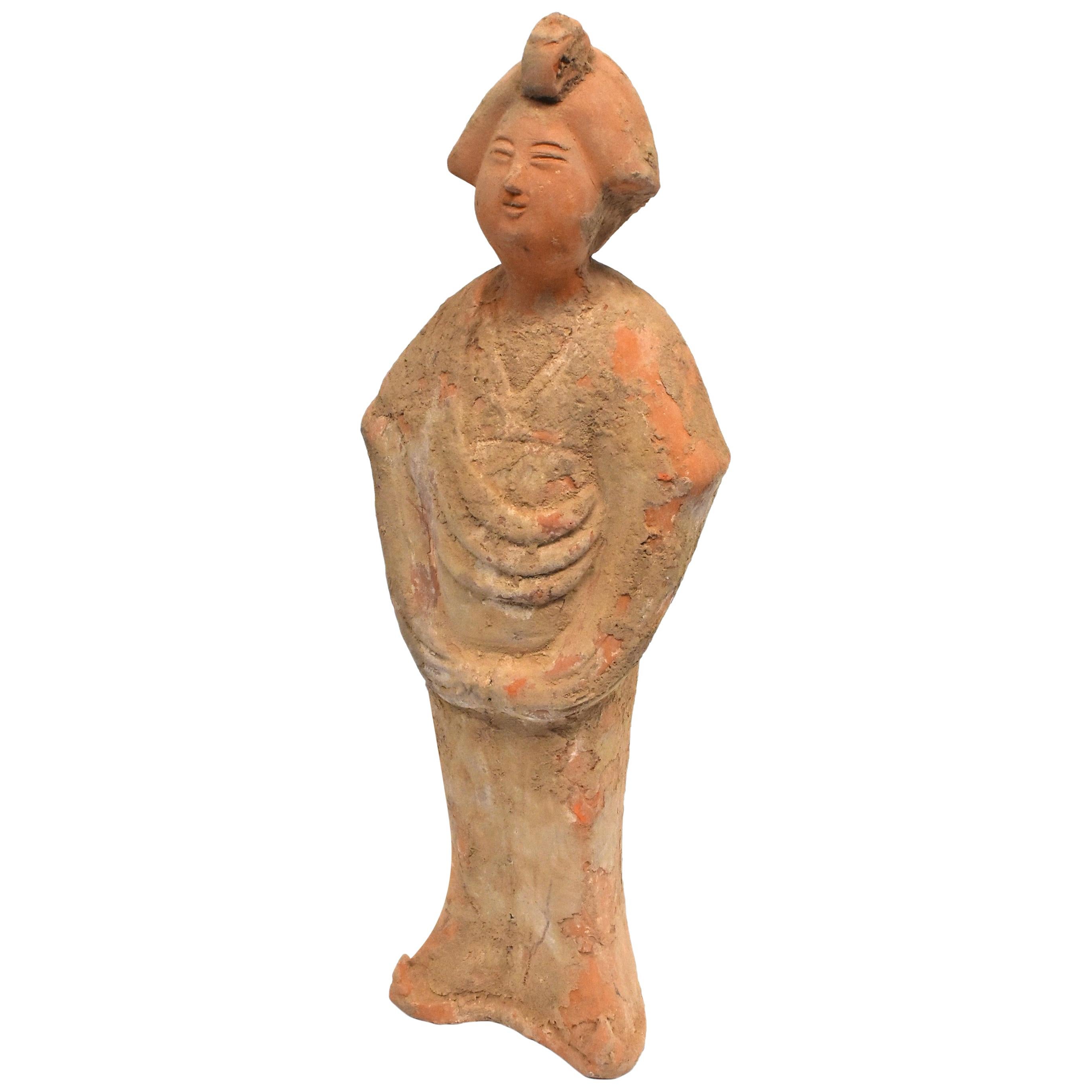 A great example of Chinese Tang dynasty pottery figure. The figure is a court lady, with a full face and traditional hair style. She Stand with both her hands behind her robe. Her face tilts up slightly and is smiling.