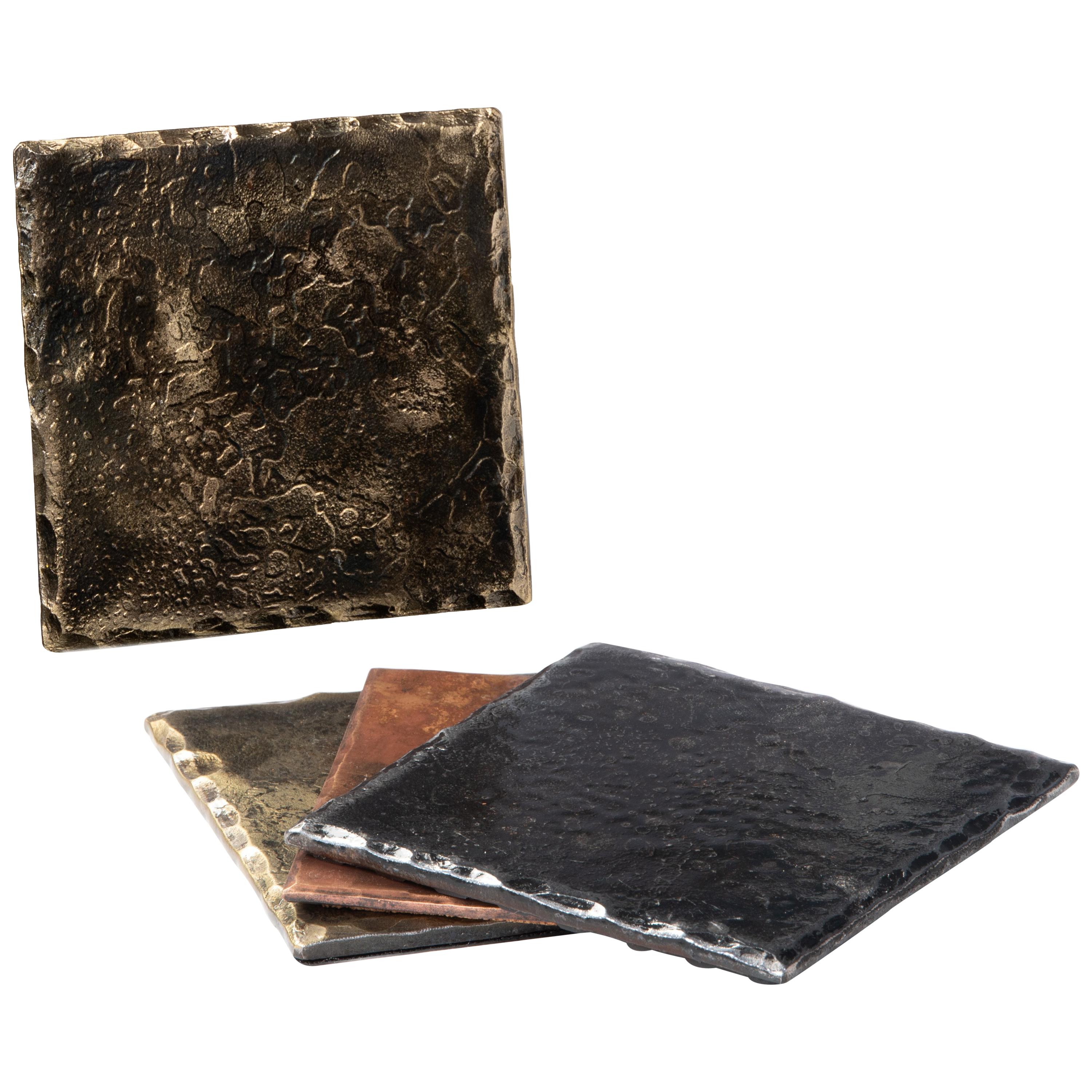 A handcrafted, steel square coaster with hammered, beveled edges. Brass highlights result in lighter gold tone that contrasts with the forge blackened steel. Wire brushed and sanded to accentuate the forged details. A glossy clear coat enhances the
