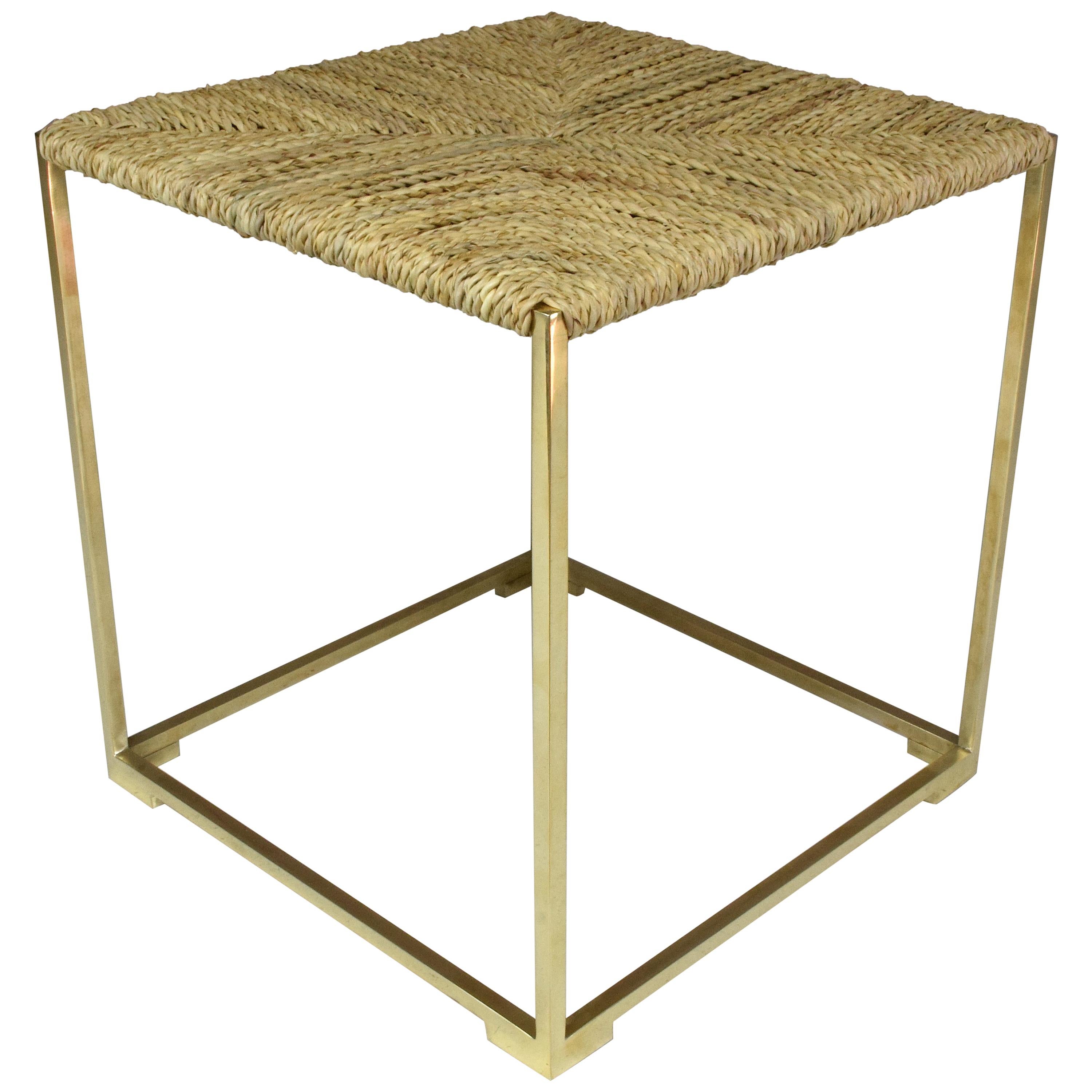 Un tabouret ou banc carré contemporain fabriqué à la main, conçu dans une structure en laiton doré - ici en finition polie - avec un dessus tissé à la main dans une fibre naturelle marocaine très résistante appelée 