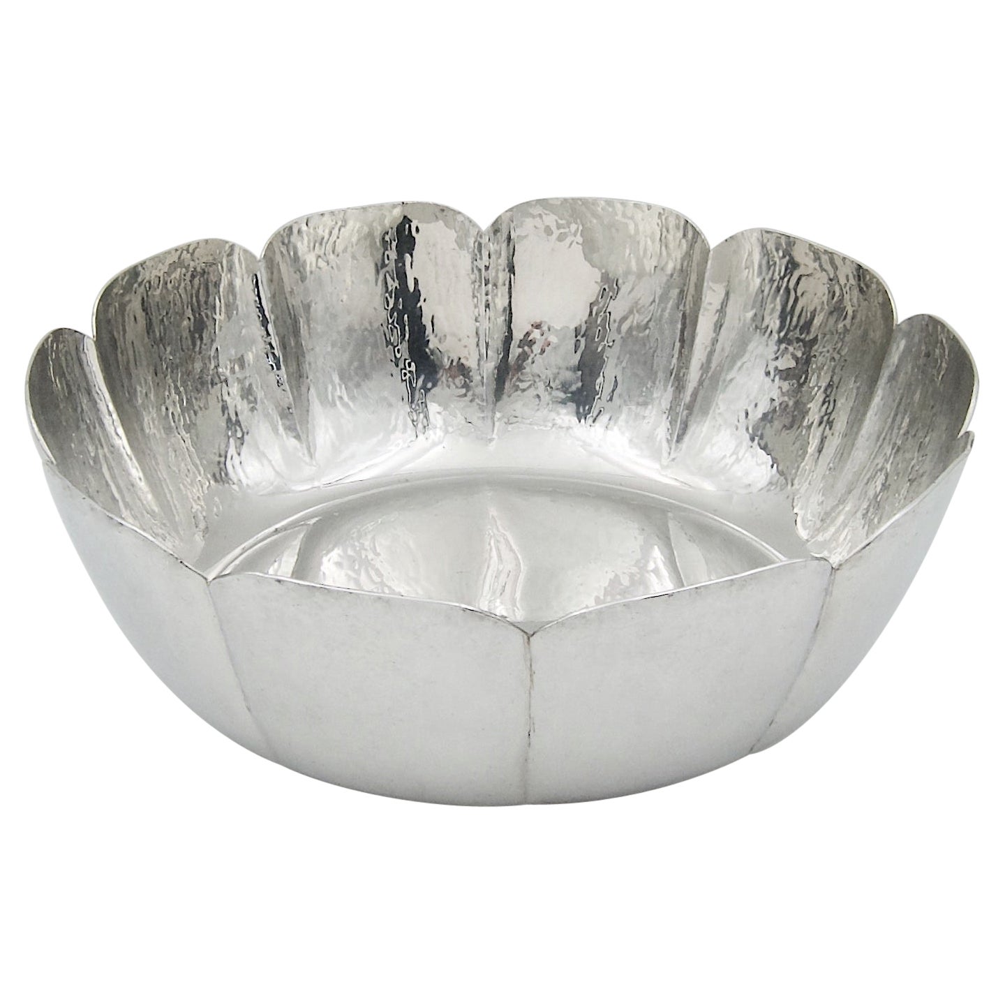 A large vintage Cartier bowl handcrafted in highly polished pewter and dating to the 1980s. The elegant silver metal design has a reflective hammered finish and fluting around the edges, flaring up and outward toward a scalloped rim. The large bowl