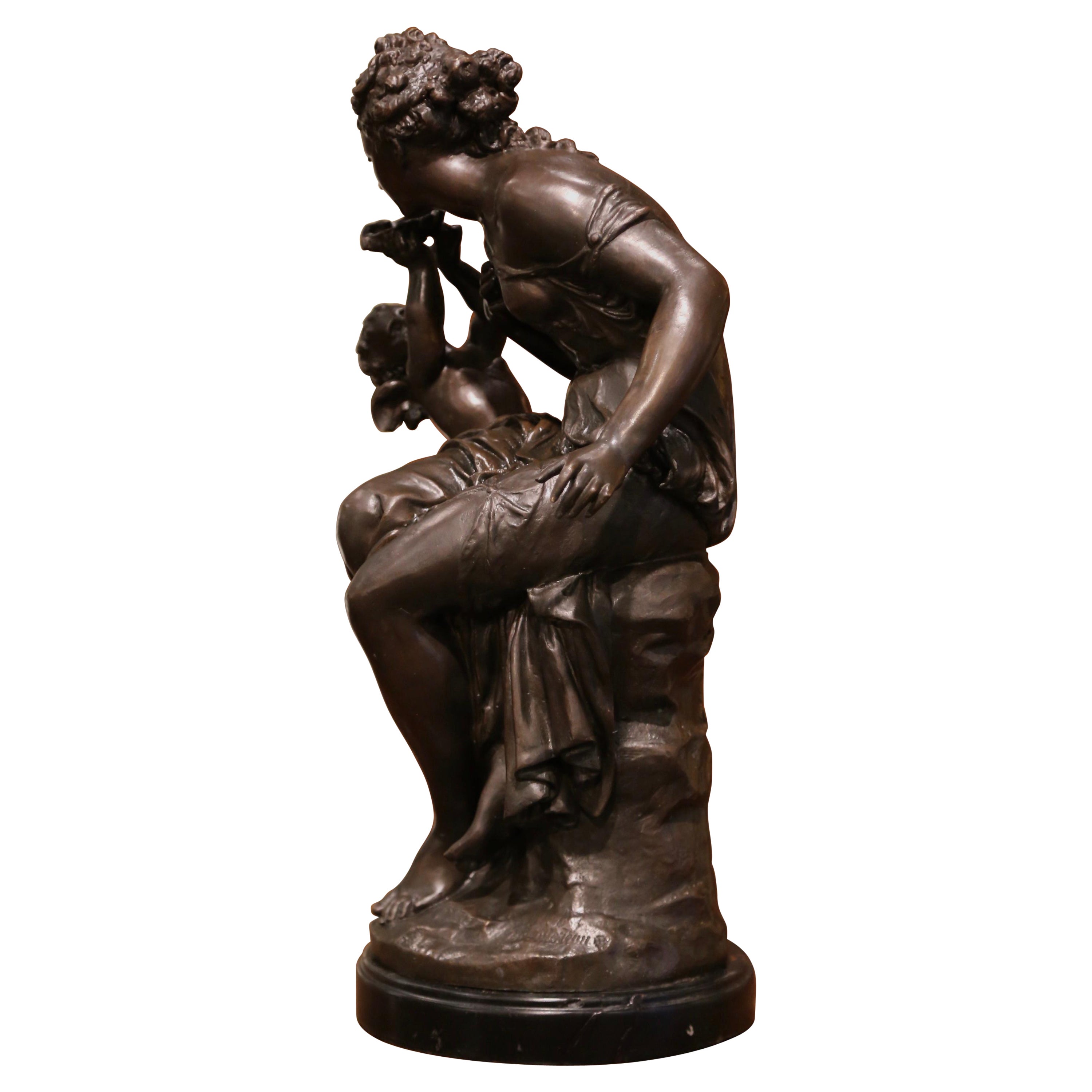 This elegant allegorical figure composition was crafted in France circa 1880; built of bronze, the statue stands on a circular black marble base, and depicts a female beauty seated on a trunk with a winged angel by her side. The tall composition