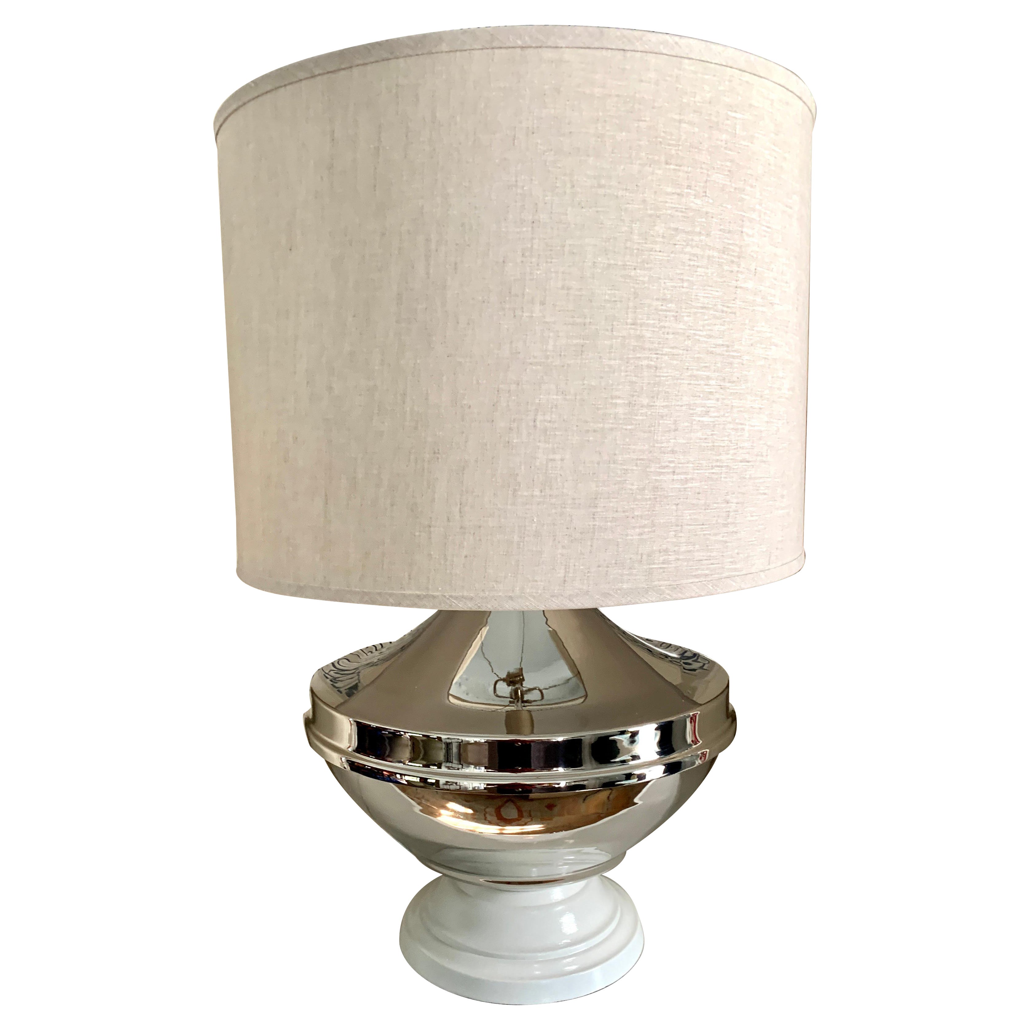 A restored mid century Chapman lamp with a large bulbous body of silver plate. The white base, and finial contrast nicely with the oatmeal linen shade. A wonderful piece for neutral interiors - the presence of this lamp is very large and is best