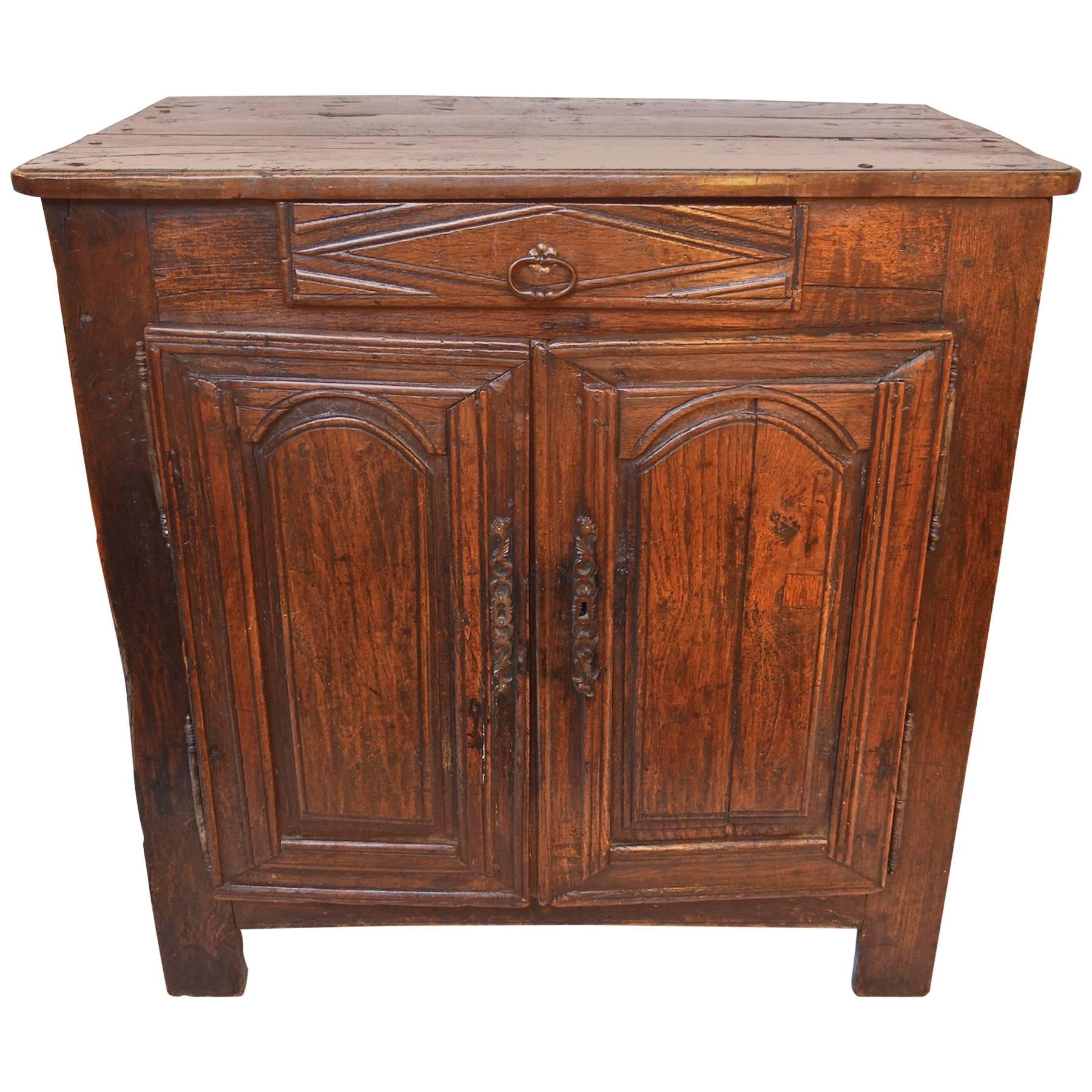 A stunning and unusual 17th century buffet of a petite size. Pegged construction of oak throughout gives this rustic, yet refined antique an incredible presence. A simple, short drawer perches above two hinged and hand-carved paneled doors. Paneled
