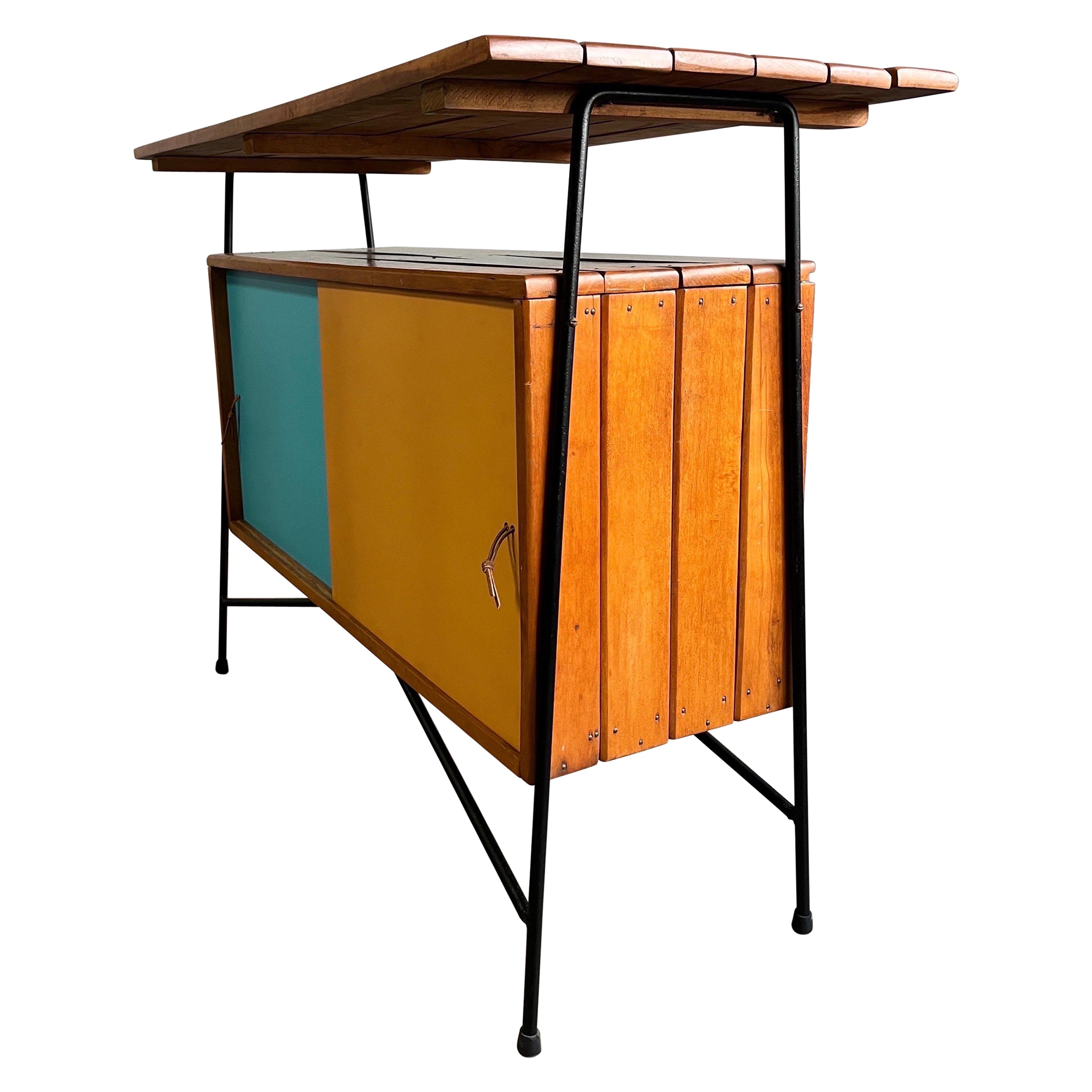 Mid-century Arthur Umanoff credenza, cabinet, or bar featuring slat wood top and lower sliding door cabinet on iron frame. Playful colored doors with sharp and dynamic lines make this piece exceptional. Can be placed against the wall as a sideboard