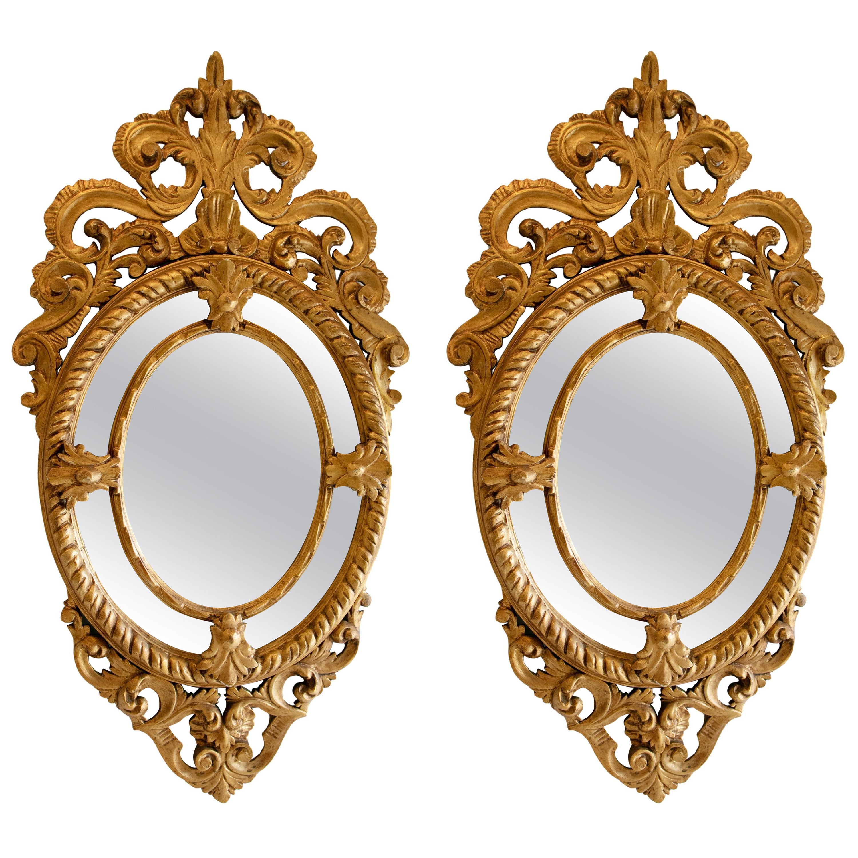 Paire de miroirs de forme ovale sculptés à la main et dorés