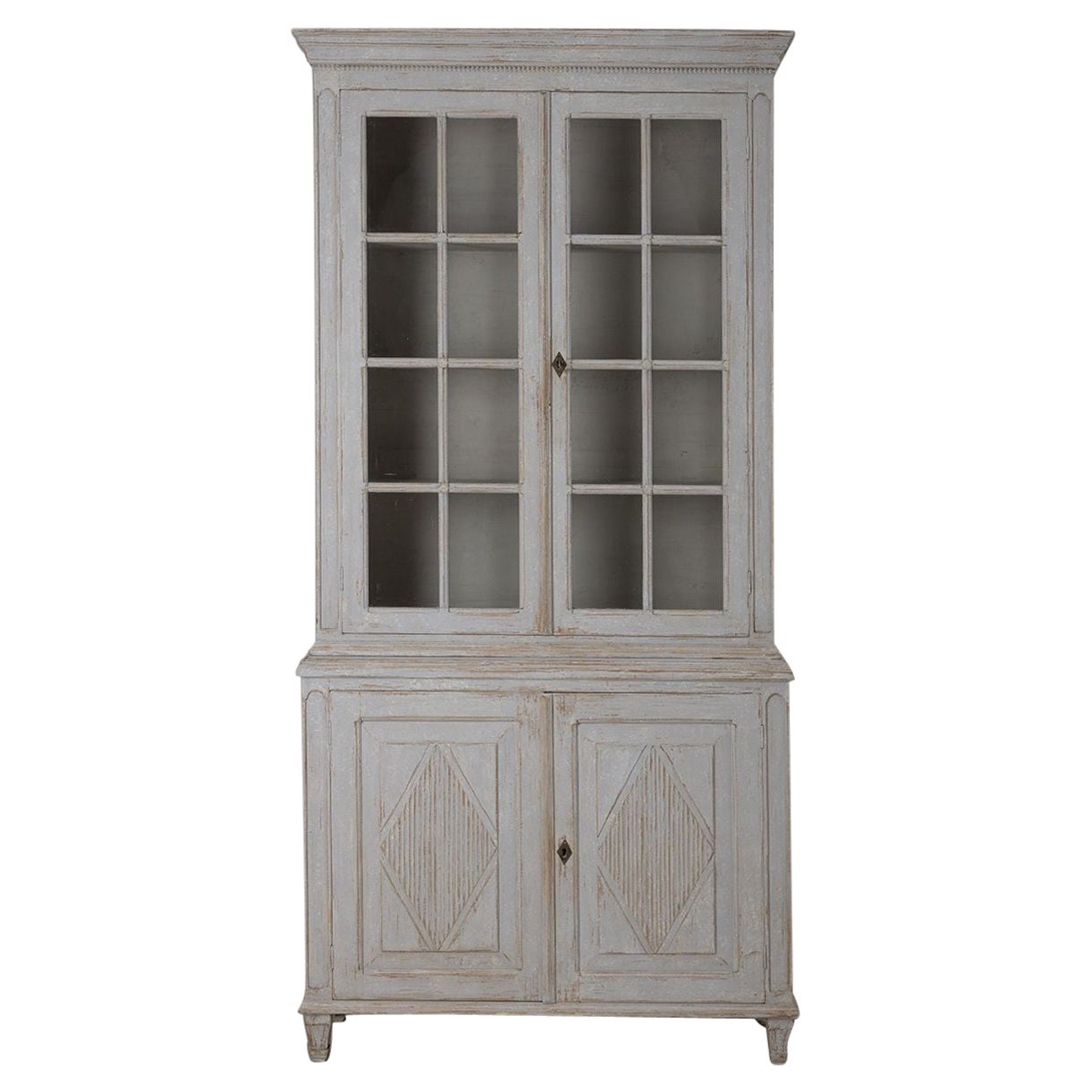 A beautiful two-part late Gustavian vitrine with original glass. Beaded molding wraps around the upper crown with 3 fixed uppper shelves and the lower doors have reeded lozenges and an interior shelf, all raised on tapered and fluted legs.