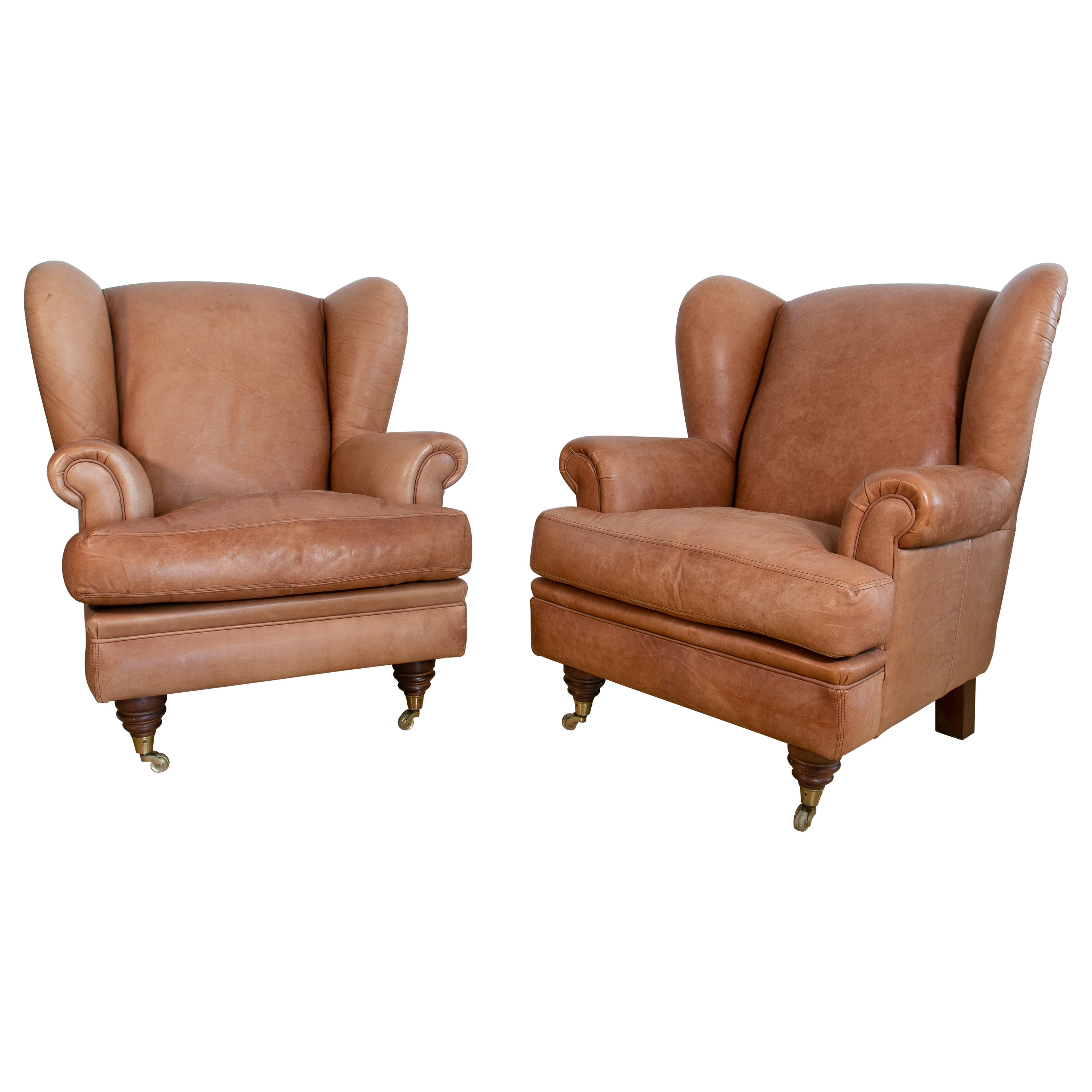 Zwei Sessel aus braunem Leder mit Holzbeinen und Messingrädern