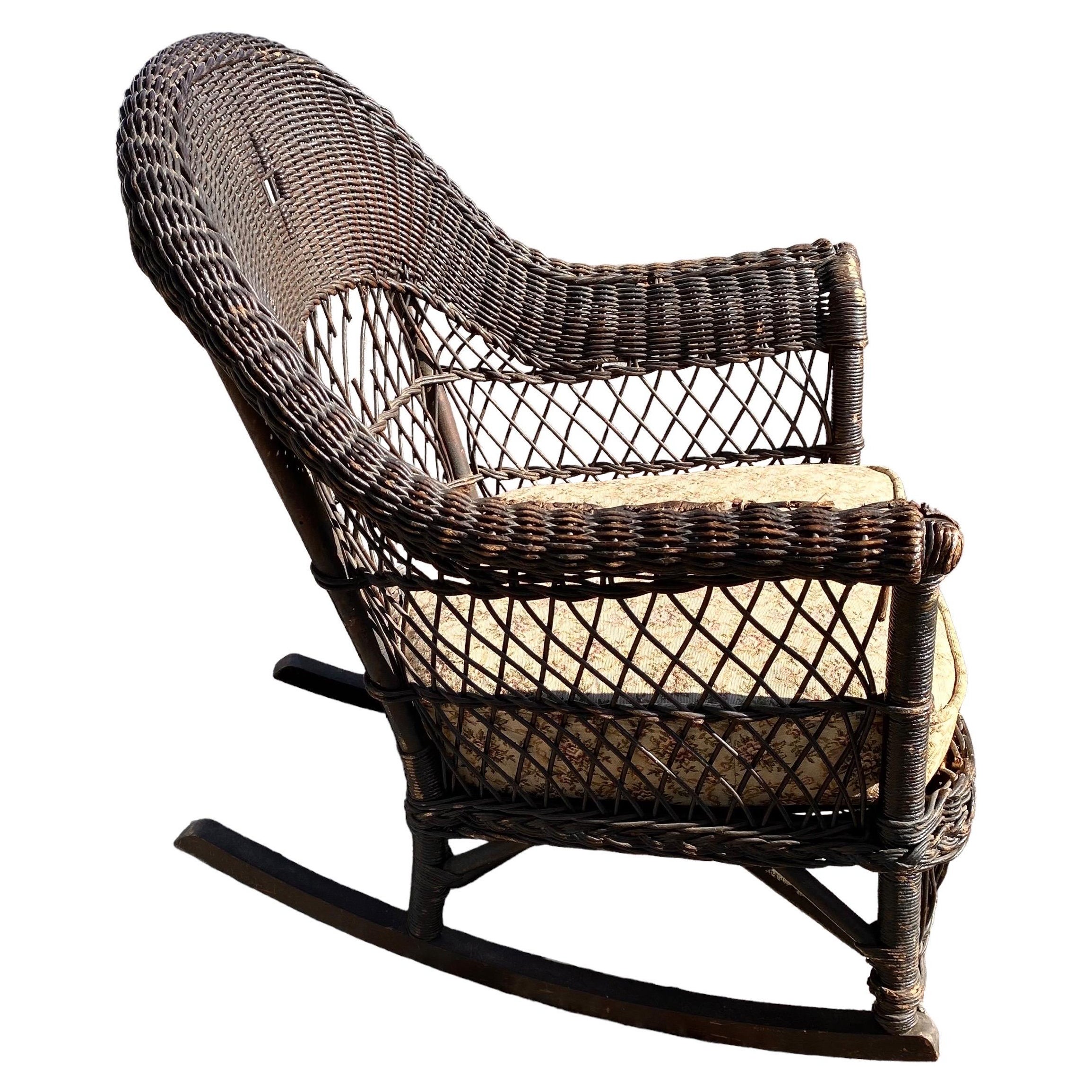 A charming early 20th century wicker rocker attributed to Jenkins & Phipps. Beautiful details and old original finish and is in remarkable condition considering its age and use, circa 1900. Would make a charming addition to your screed in porch or