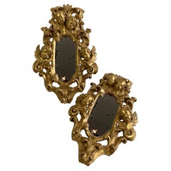 Un par de espejos de madera dorada con querubines