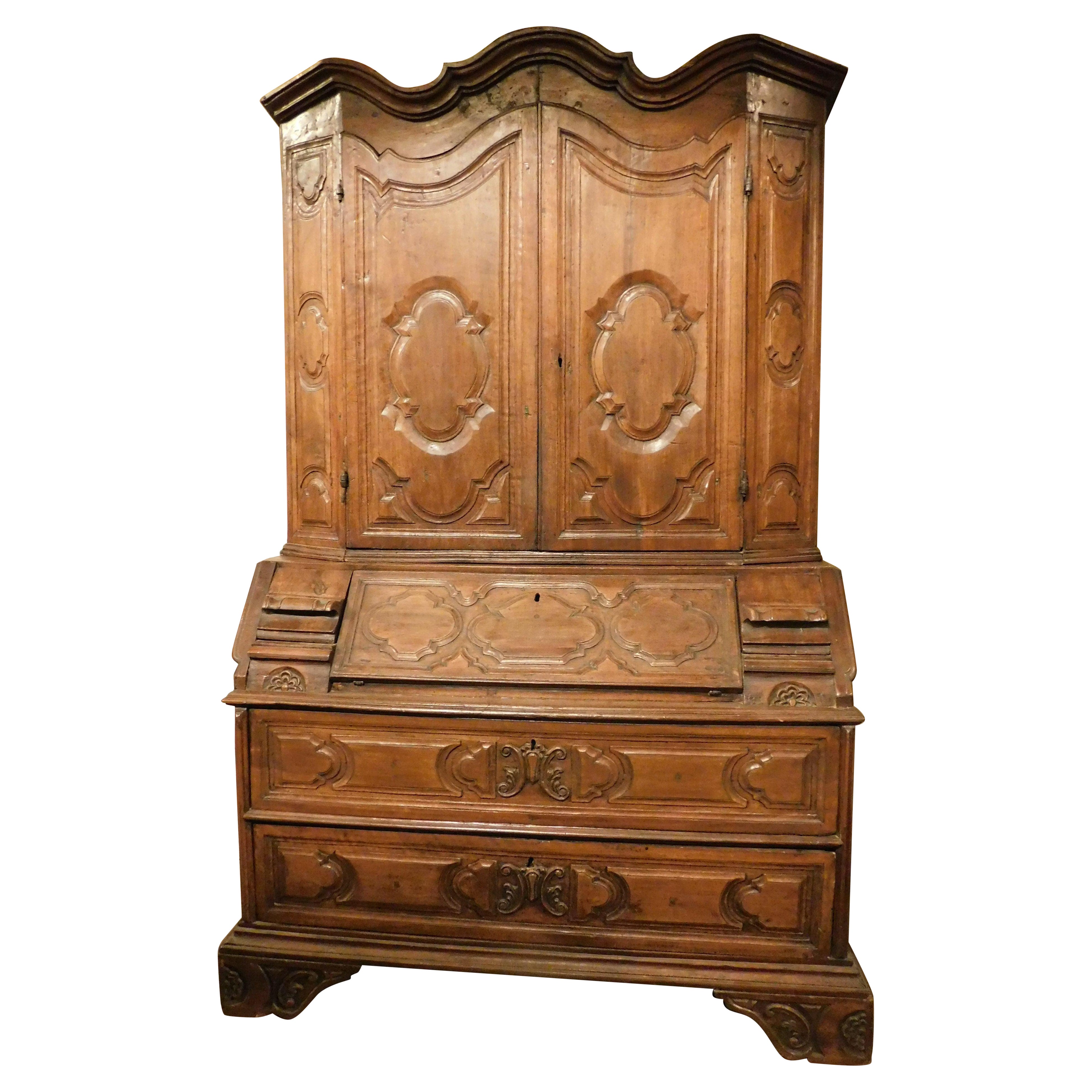 Trumeau, double body in carved walnut with doors, flap and drawers, Italy