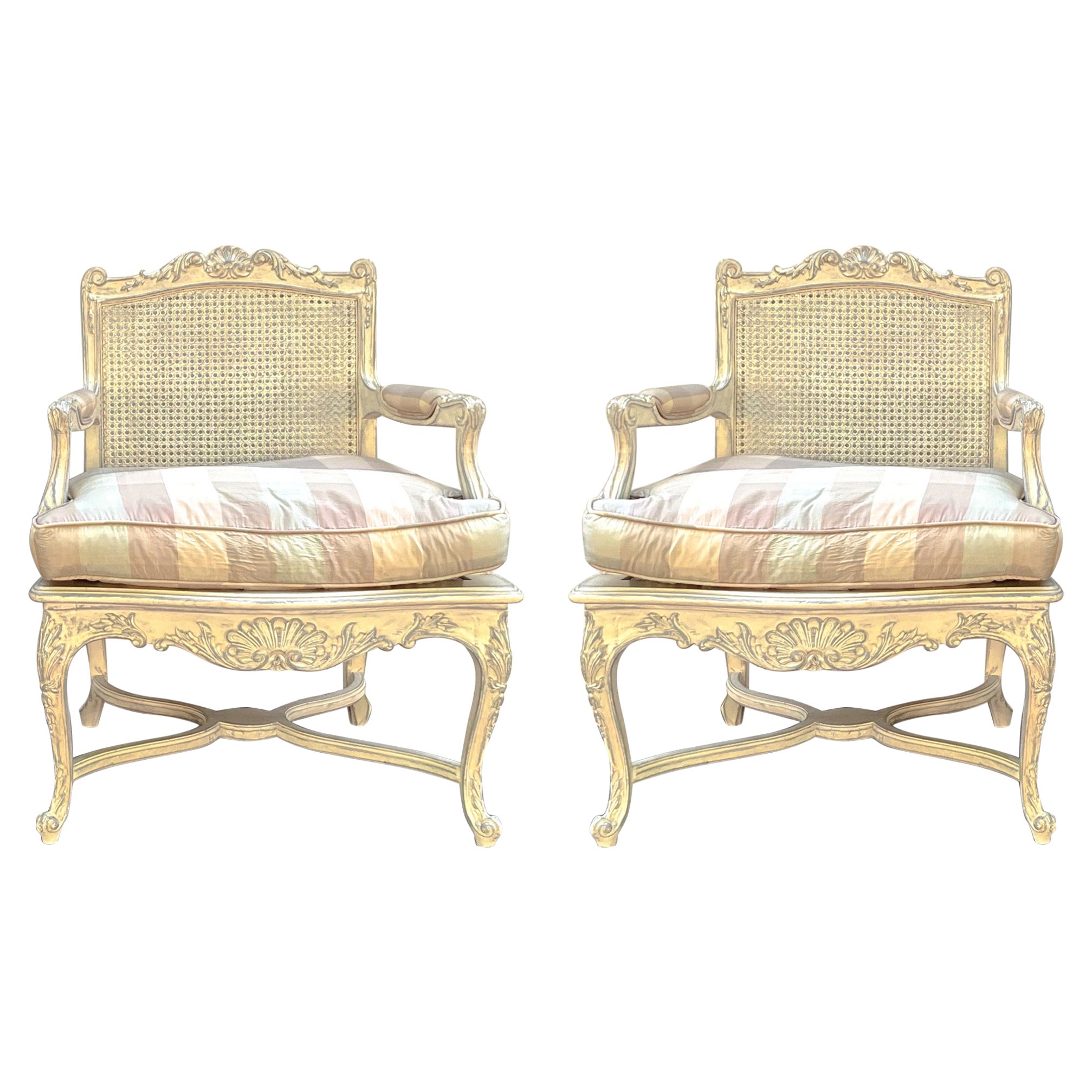This is a lovely pair of French Louis XV style caned bergere chairs with vintage check upholstery. The upholstery feels like silk but could be a blend. The frames are ivory painted with gray accents. The seat without the cushion is 16”. The arm is