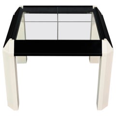Postmoderner Beistelltisch mit schwarz lackiertem Rahmen und cremefarbenen, weißen Trapezbeinen und Glasplatte