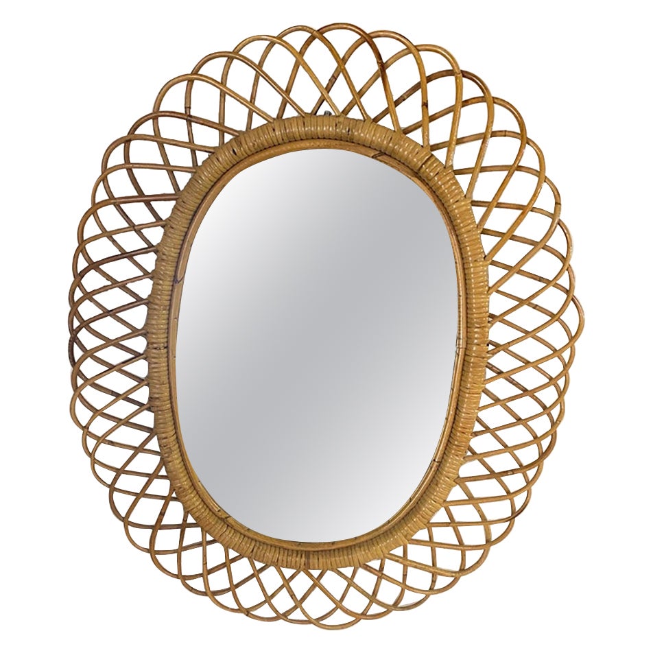 Italian rattan wall mirror (circa 1960s) by Franco Albini. The mirror has a complex weave of rattan in a series of horseshoe projections on the edge of the frame. There is a lovely aged patina on the rattan; the glass is intact.