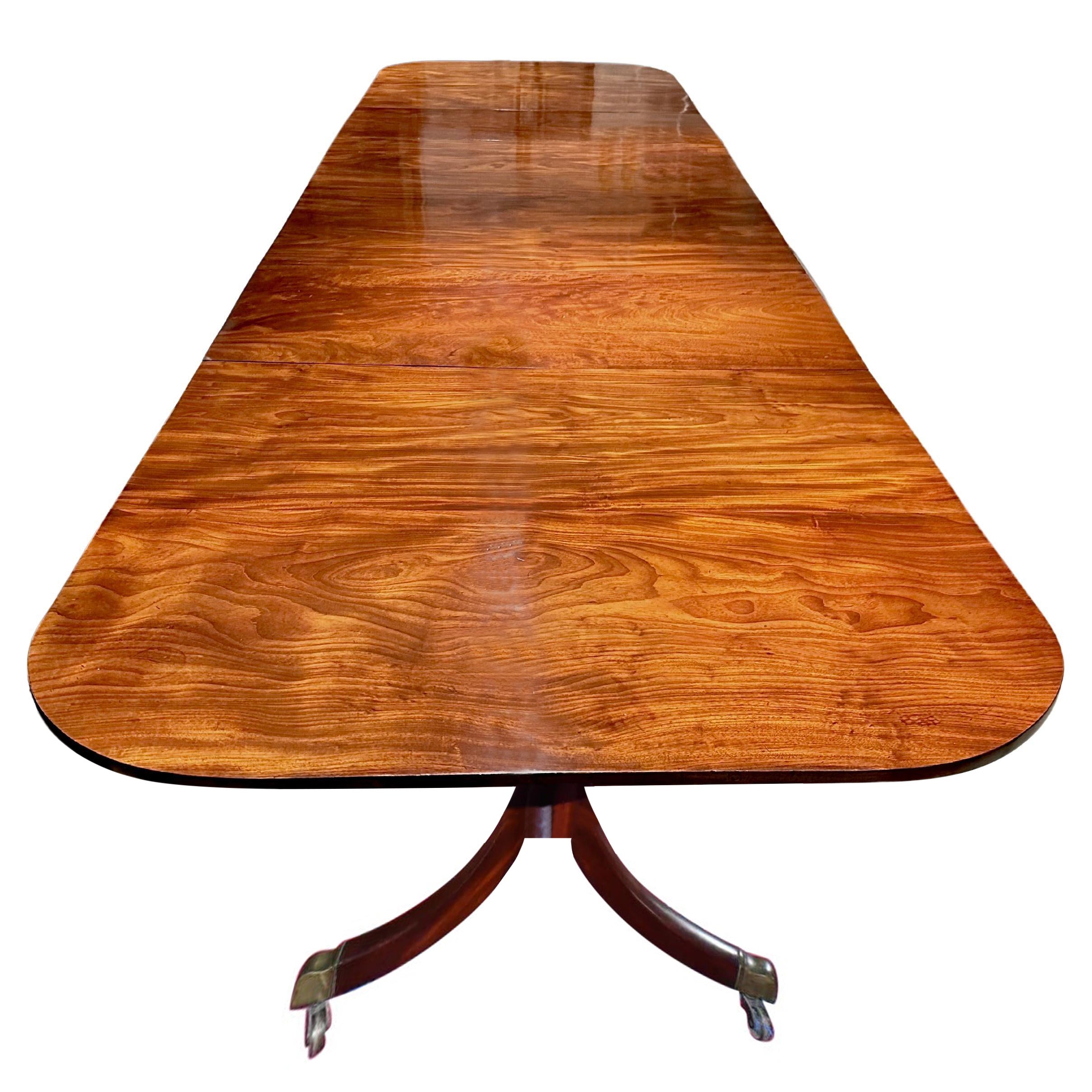 An exceptional George III or Regency mahogany triple pedestal dining table with two additional leaves.   The rectangular top having rounded corners, each top of three fine richly grained and colored mahogany boards tilting above three pedestal bases