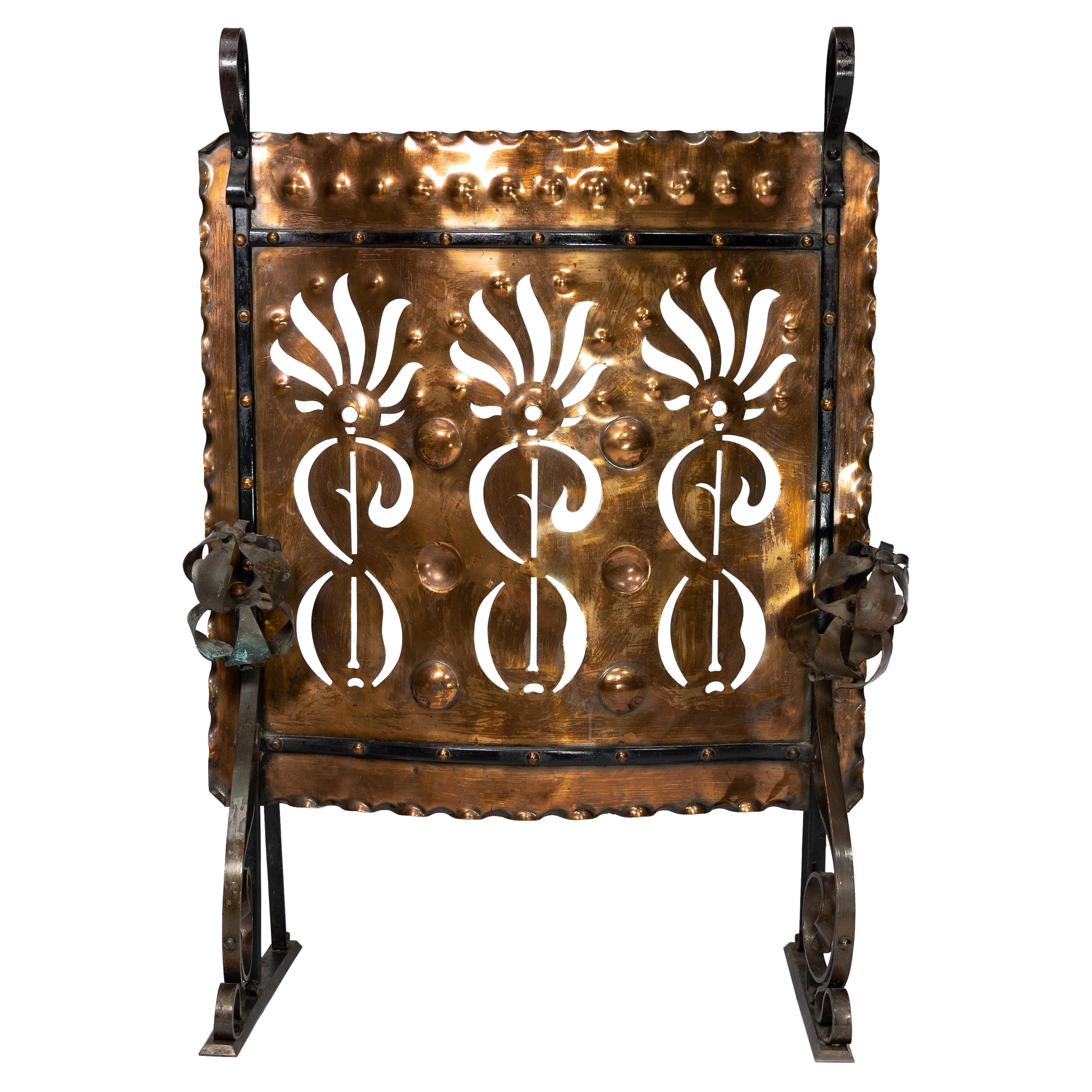 Liberty and Co. An Arts and Crafts wrought iron and copper firescreen with perced floral decoration and flower heads to the front with scrolled iron work to the frame and feet.
