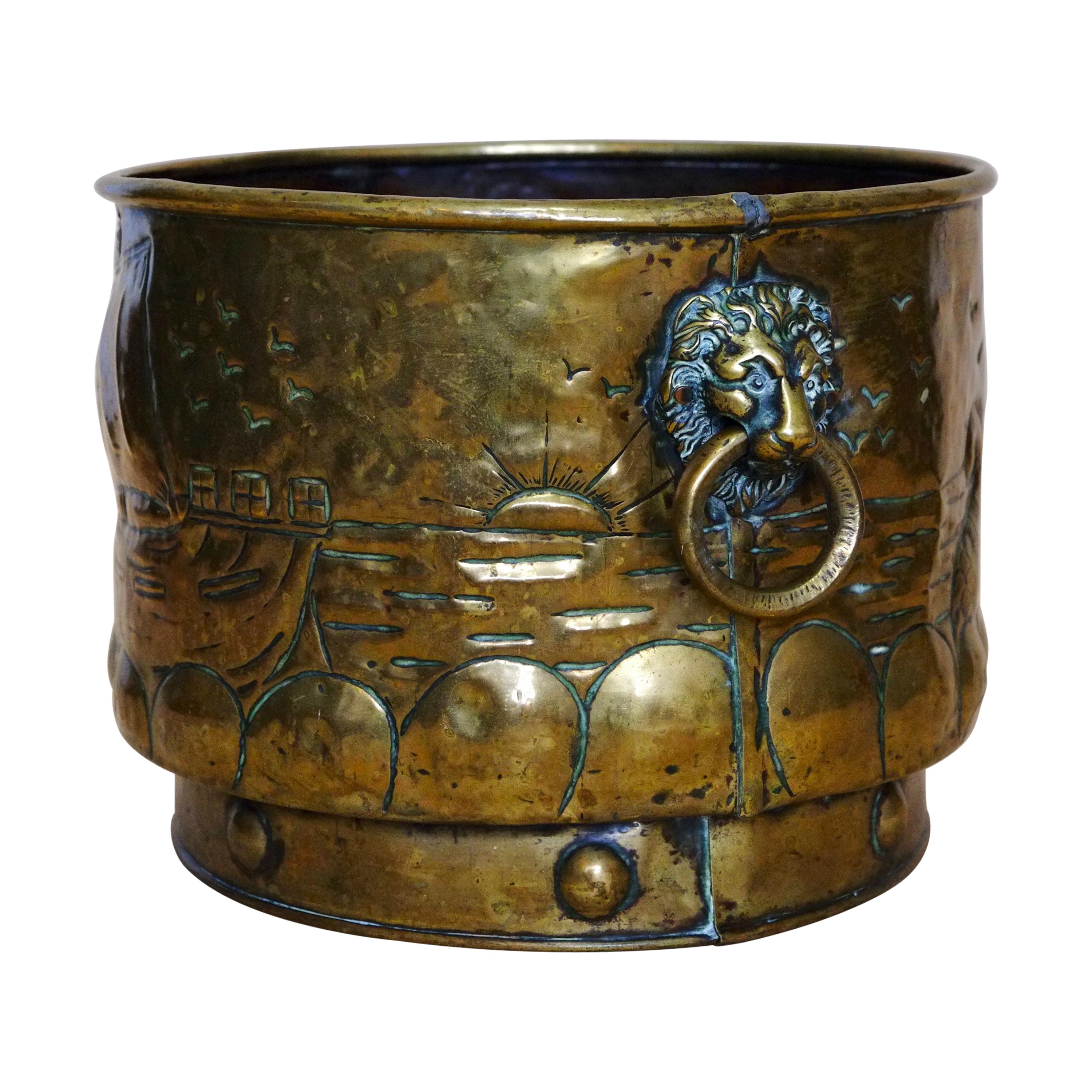 Extra large solid brass log bucket. England circa 1880. A gorgeous antique piece with lion head handles and a decorative viking ship hand embossed motif. This bucket has a deep collared base with circular decorations. Lots of character and patina.
