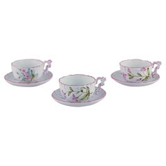 Three hand-painted tea cups and saucers in faience with motifs of flowers.