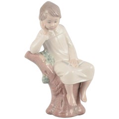 Lladro, Spanien. Porzellanfigur eines Mädchens, das auf einem Baumstumpf sitzt. 