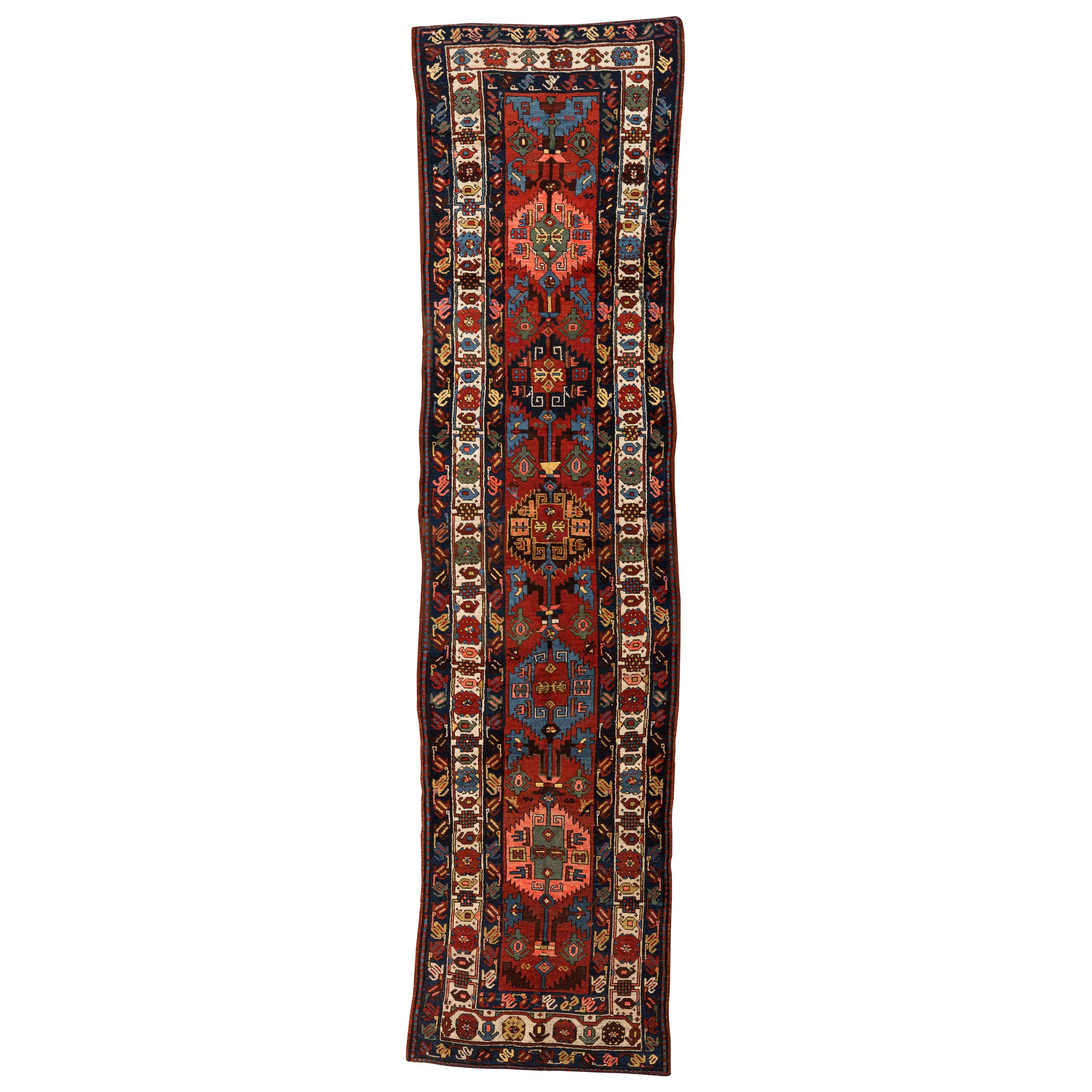 Kazak - Northwest Persia
This is an antique Kazak runner with vibrant colours and bold design. The red field features five complete, serrated medallions interconnected by rose buttons and rectilinear floral branches. Geometric figures, including