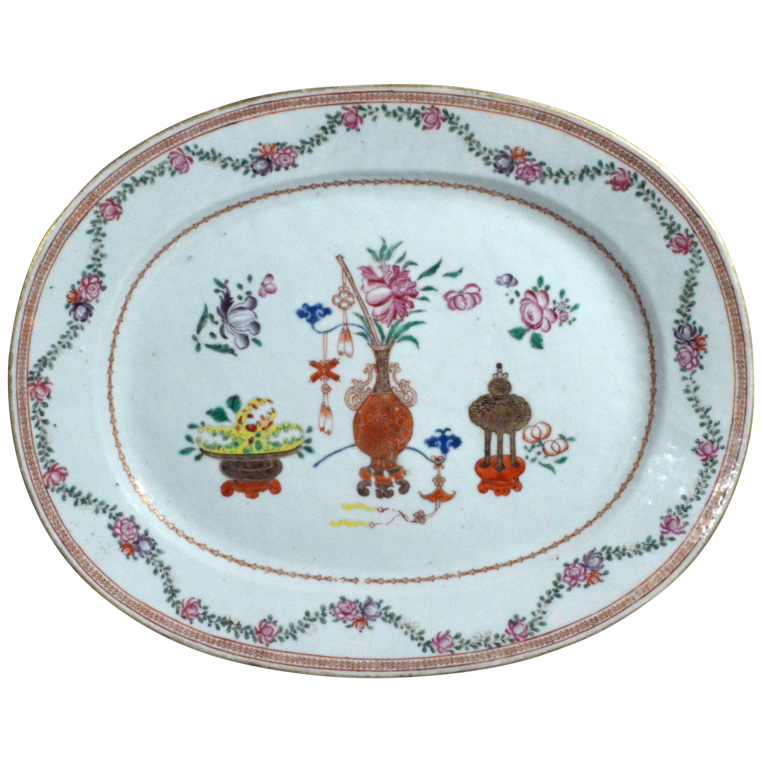 The Chinese Export porcelain dish in the famille rose palette is painted on the border with meandering vines and flowers which surrounds a central panel decorated with vases and pots of flowers.
  
