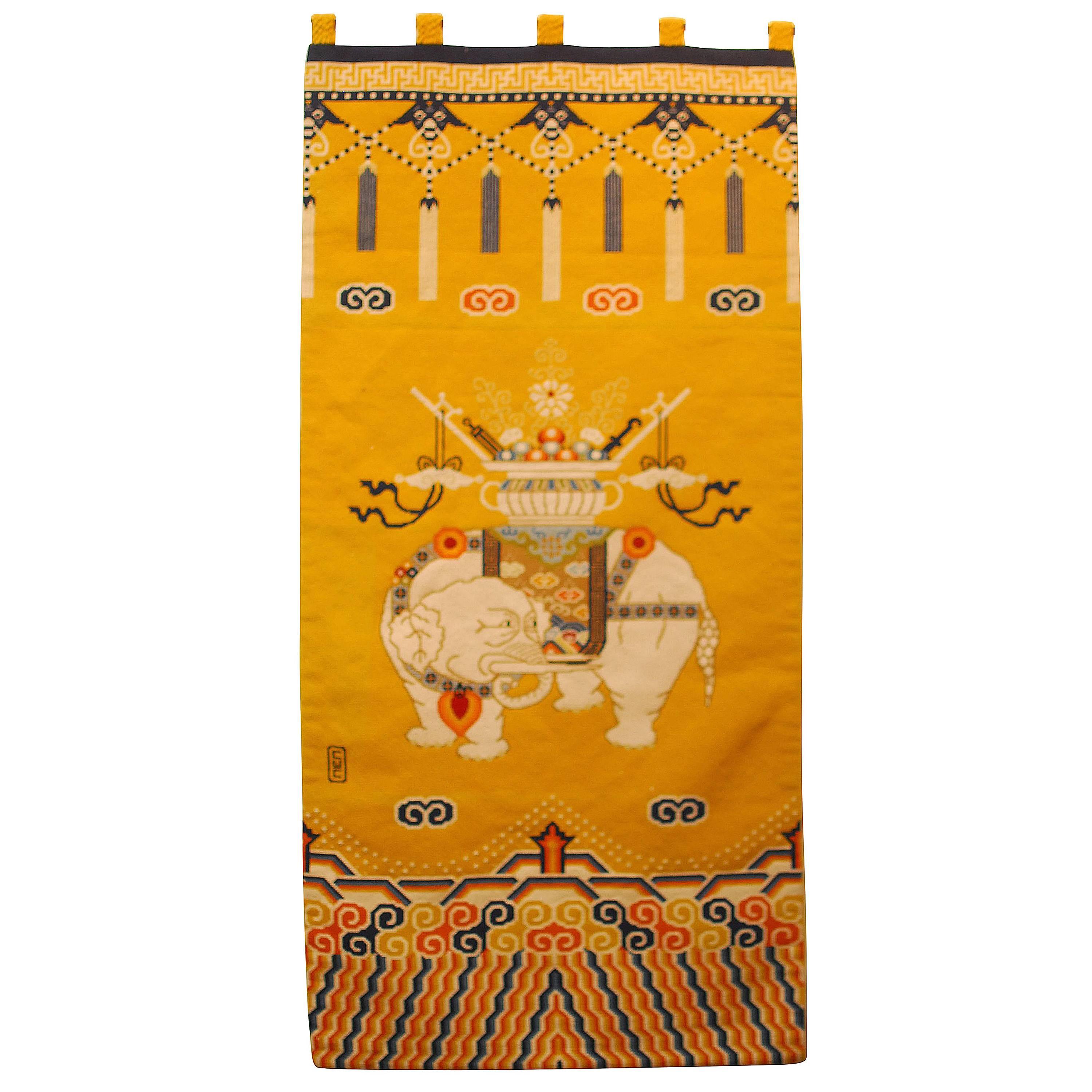 Colorful Tibetan Khaden style needlepoint rug featuring a white Asian elephant and decorated with geometric patterns of Greek keys and cloud motifs. The top depicts long tassels hanging from beast heads. The carpet has a bright yellow background and