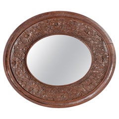 An Arts & Crafts walnut circular mirror with stylized floral carved decoration