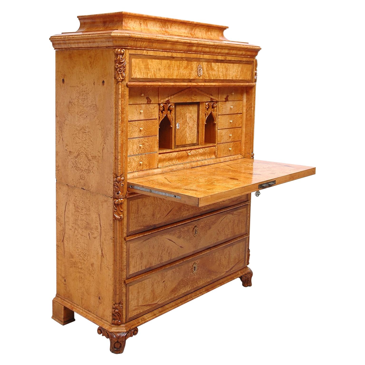 A handsome secretary abattant in birch, with birch root on drawer faces bordered in walnut. Offers a long drawer below pedestal top with desk top opening to many small drawers with two open compartments flanking a closed center cubby. Three large