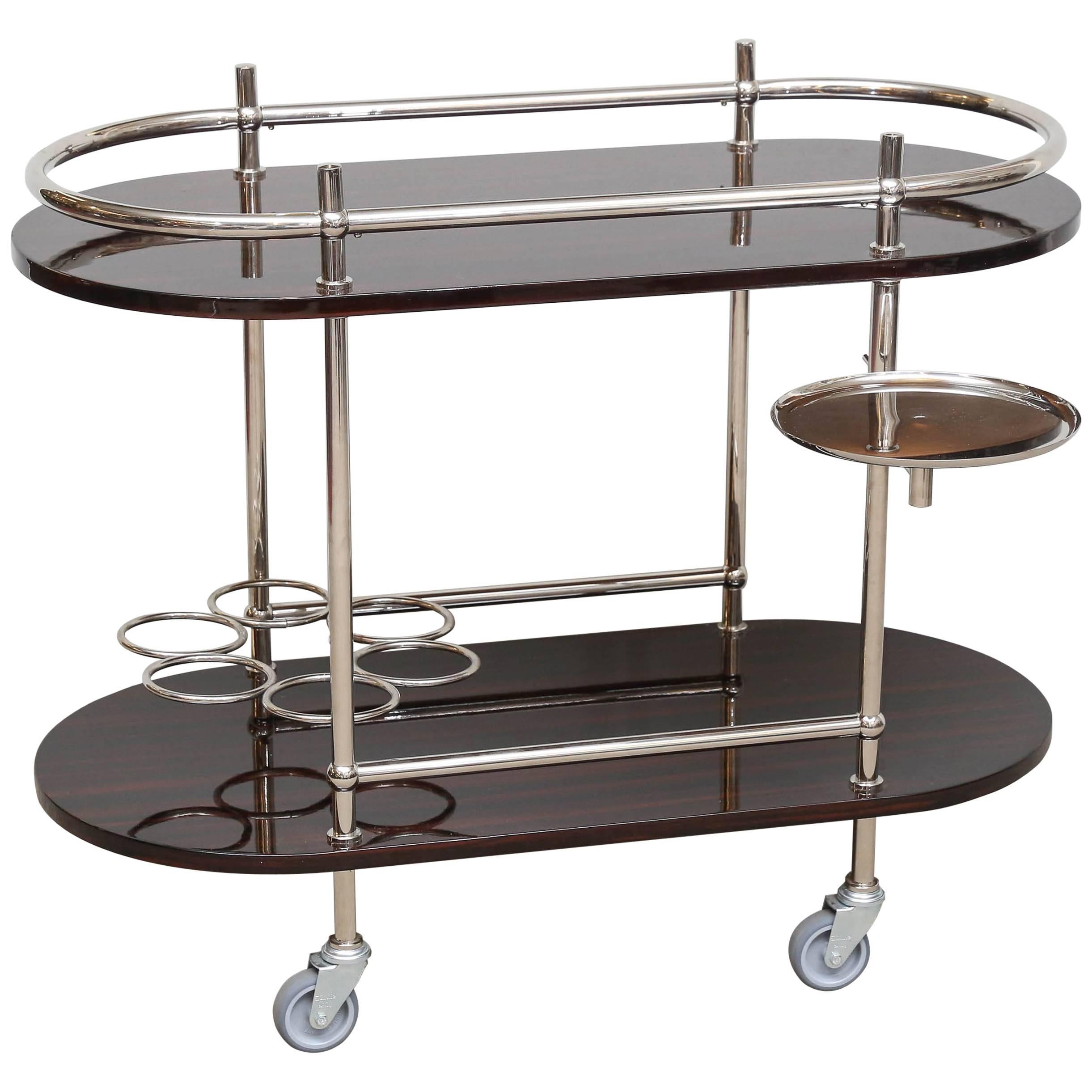 Oval veneer wood top tray rests above a smaller oval shaped base tray. The cart is held together with chrome tubing supports, which also utilized as rails and shaped into glass or bottle holders. There is a build in ice bucket holder that folds in