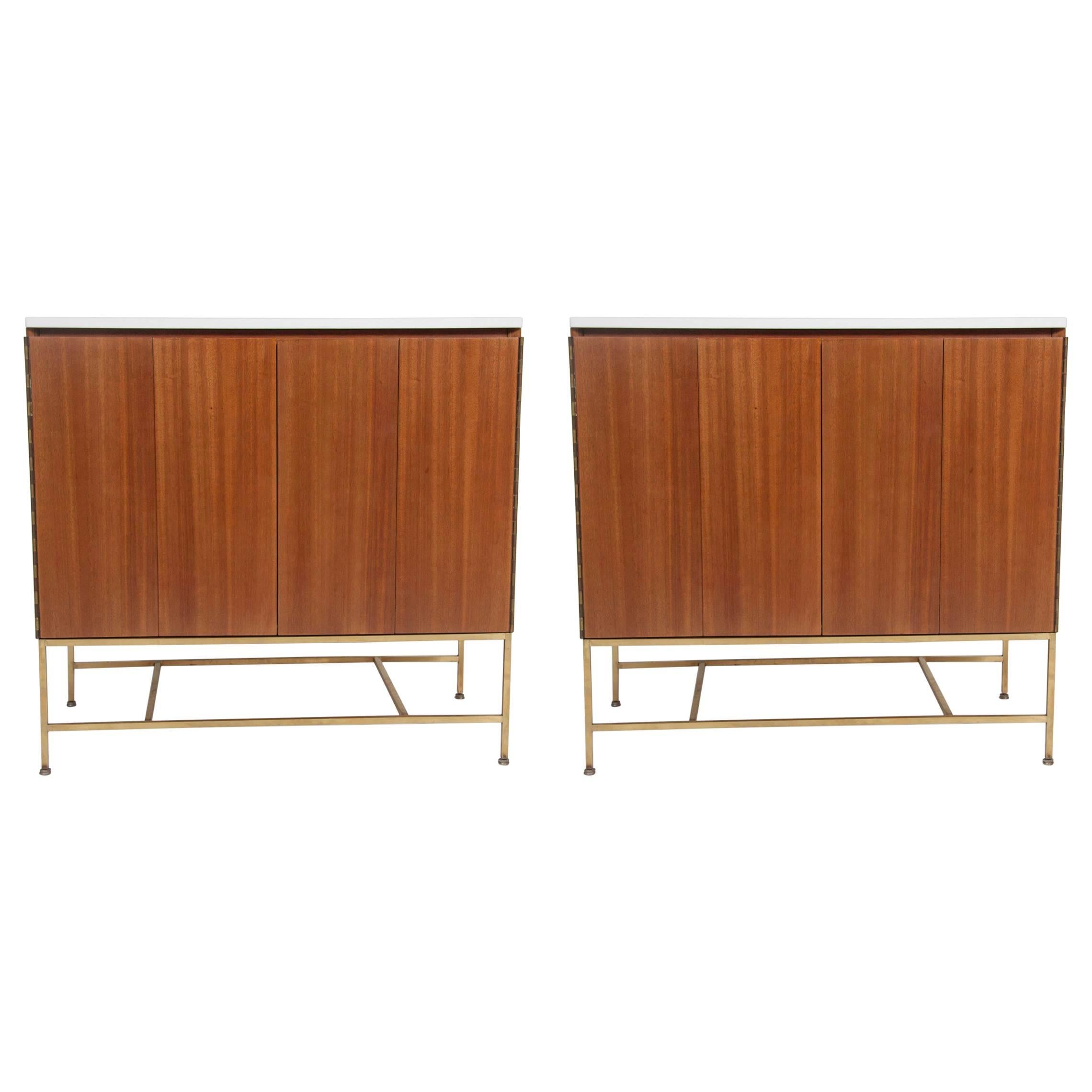 A pair of Paul McCobb bedside tables with period Vitrolite white glass tops made by Calvin.   The cases have two bi-fold doors each and a single drawer over one shelve.   Both cabinets are raised on brass armatures.  