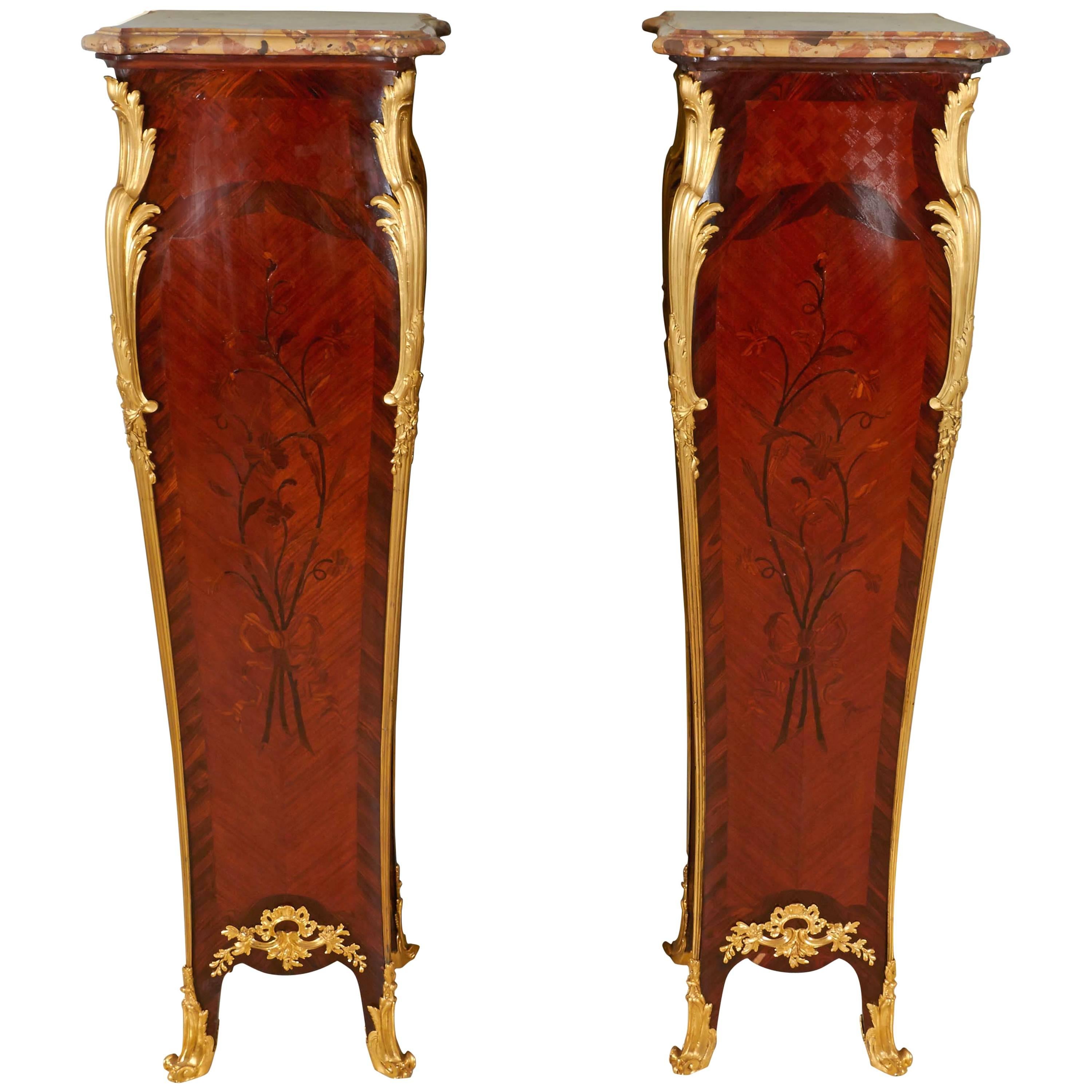 A pair of French ormolu-mounted kingwood marquetry pedestals by Maison Millet. With original marble tops.

The serpentine square breche d'Alep marble top with moulded edge, over bombe form case with cube parquetry, floral marquetry and book