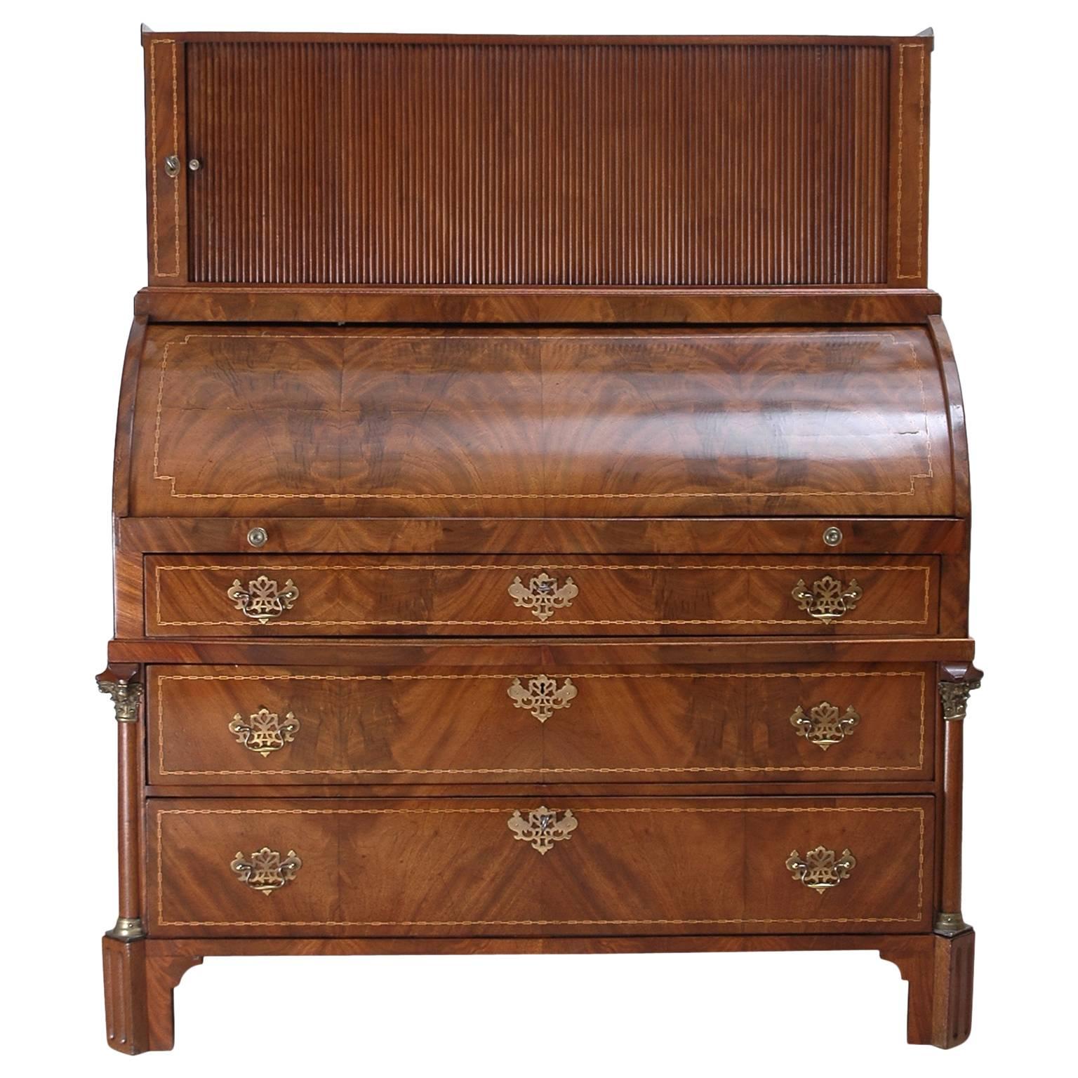 A Louis XVI secretary desk in mahogany with satinwood inlays. Offers a cylinder top that opens to reveal a series of small drawers surrounding a closed cubby by pulling on the writing surface by way of two brass pulls. Above desk top is a tambour
